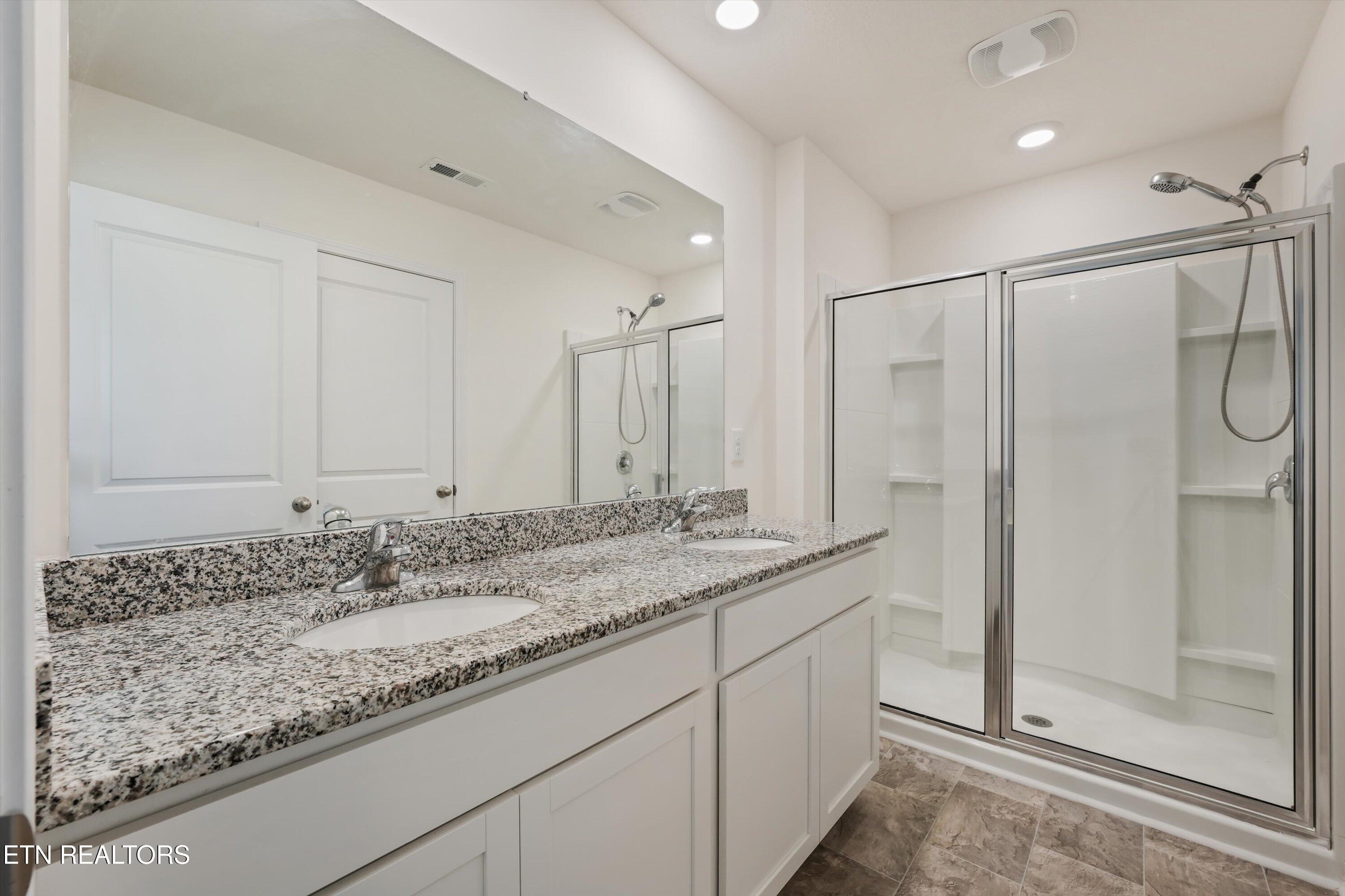 Bathroom with a granite double vanity and a glass-enclosed shower with built-in shelves.