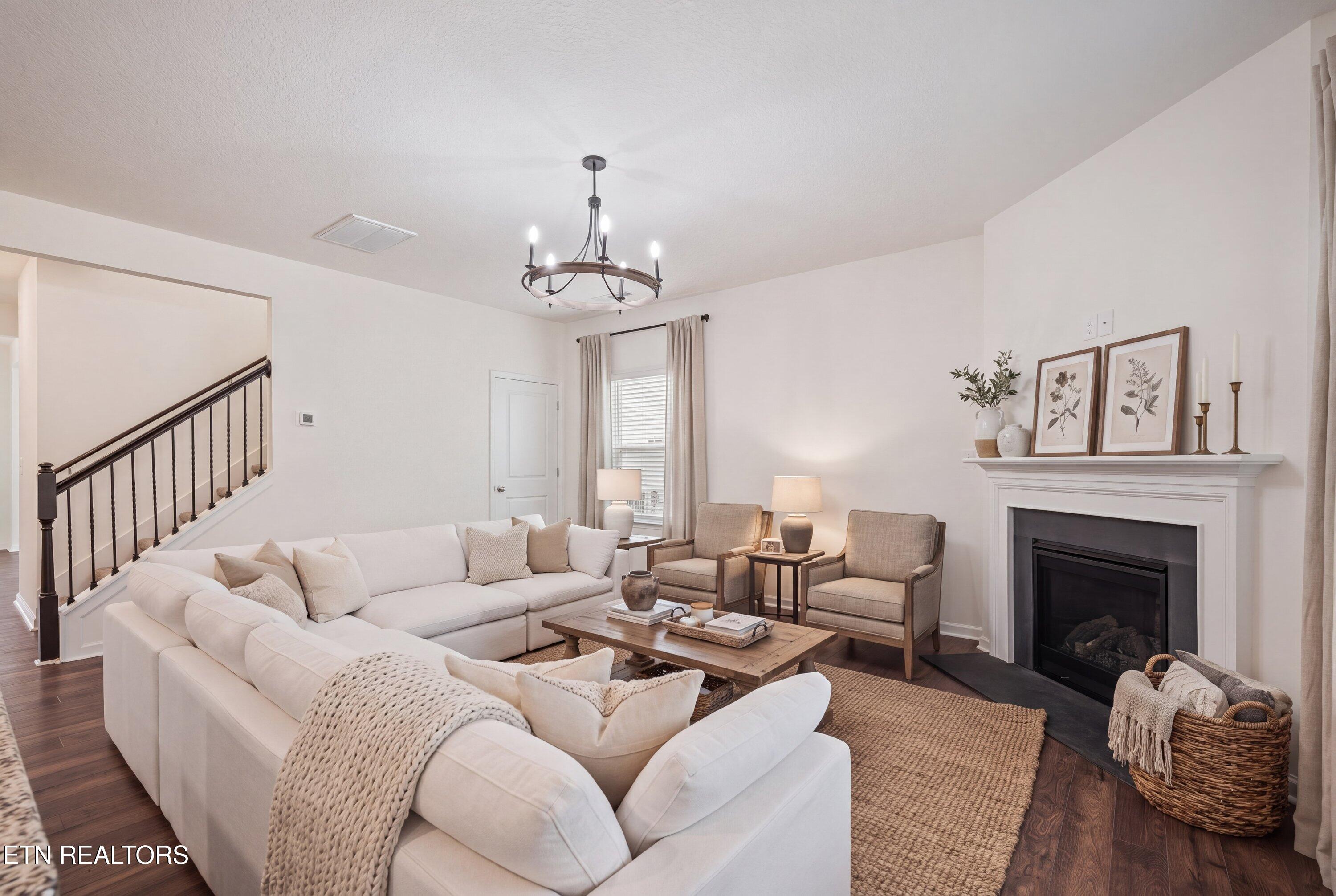 Living room with a white sectional, woven rug, and white fireplace beside a staircase.