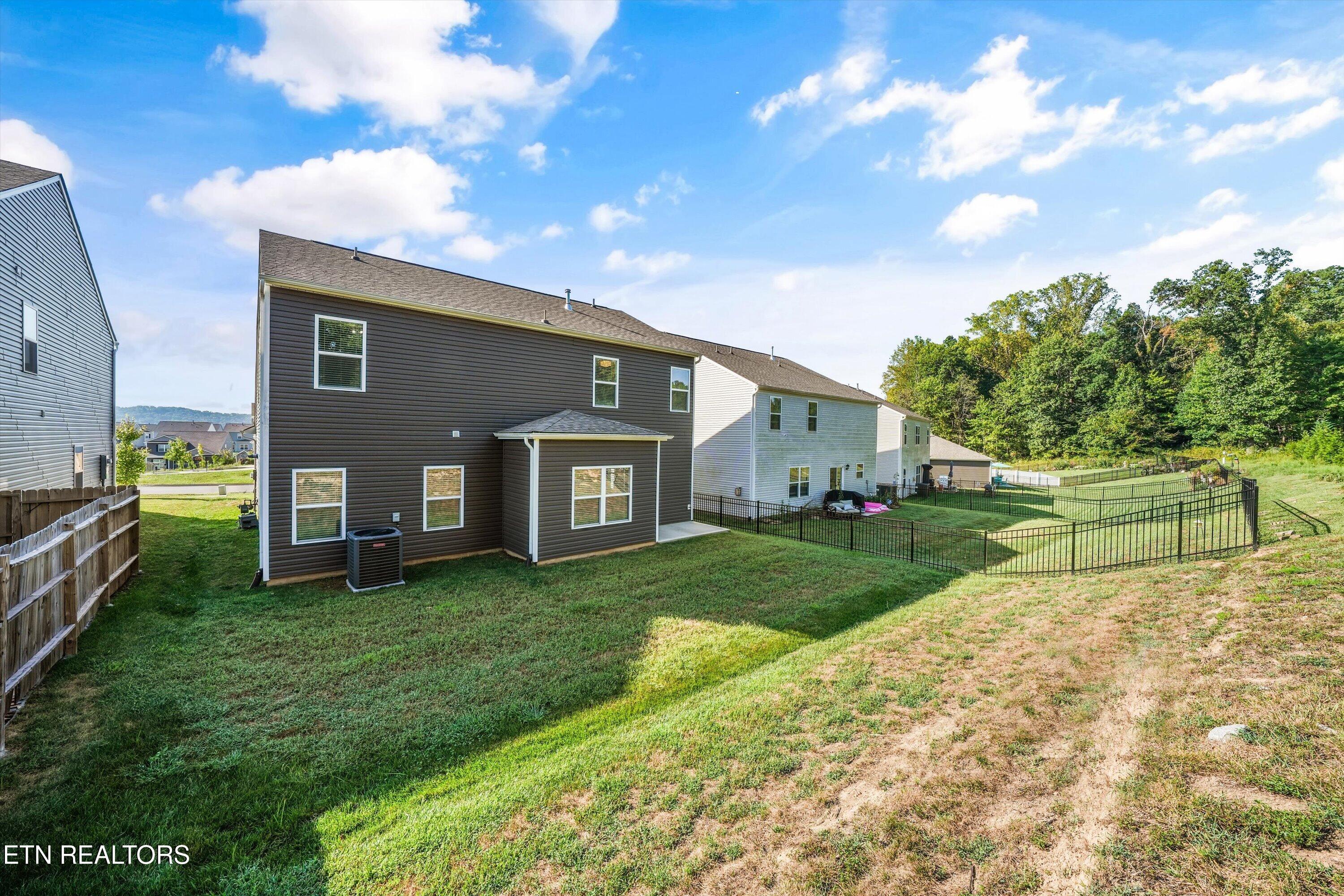Rear of a two-story brown-sided home overlooking a sloped backyard, with a covered patio and fenced area.