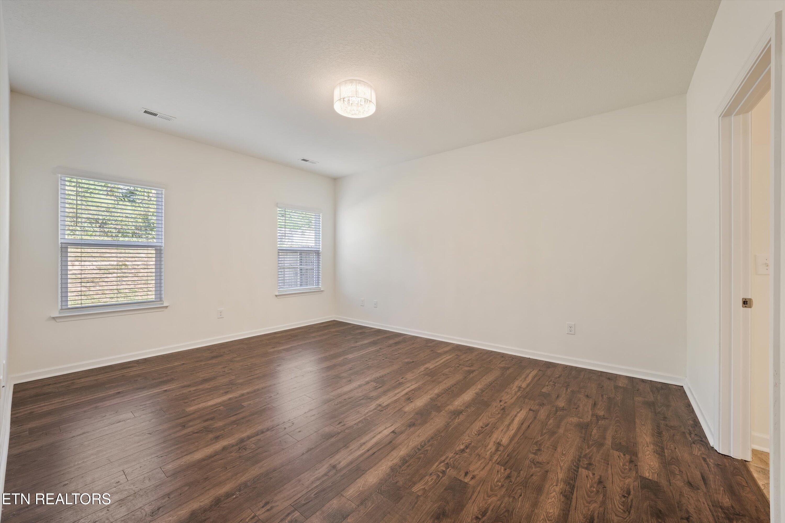 Vacant bedroom with dark hardwood floors, two blind-covered windows, and a ceiling light.