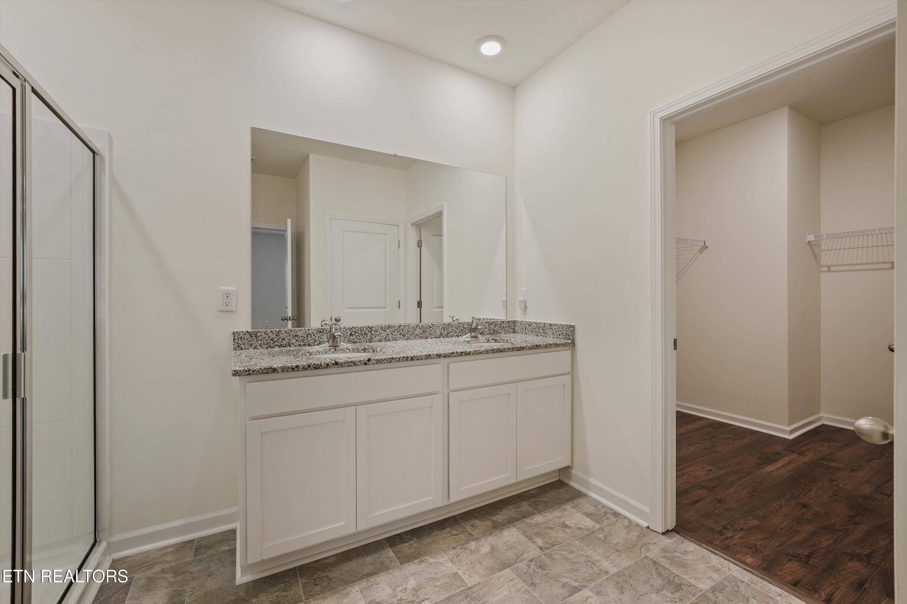 Bathroom with double-sink vanity and granite counter beside a glass shower and walk-in closet.