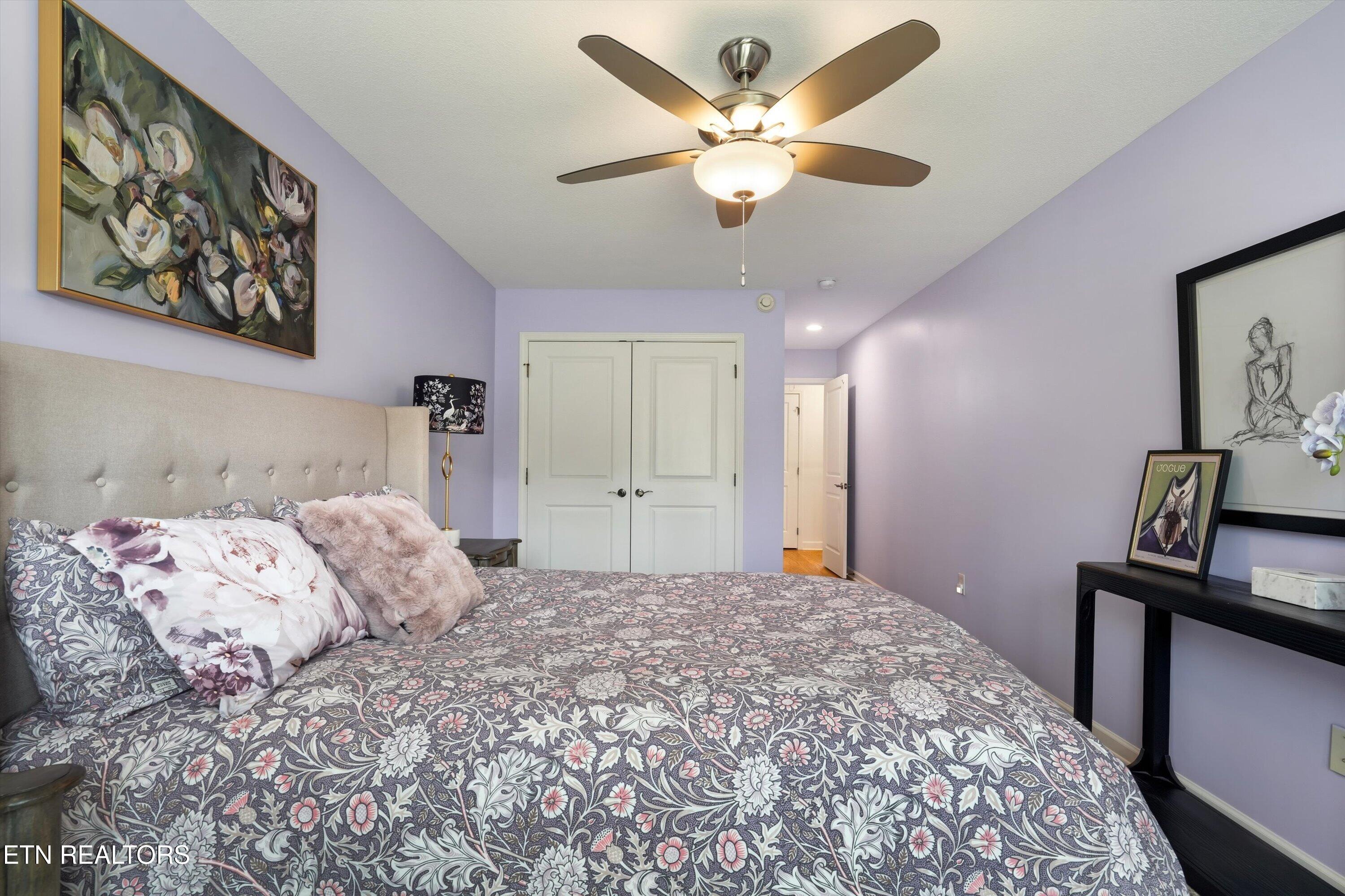 Bedroom with lavender walls, floral bedding, a tufted headboard, and a lit ceiling fan.