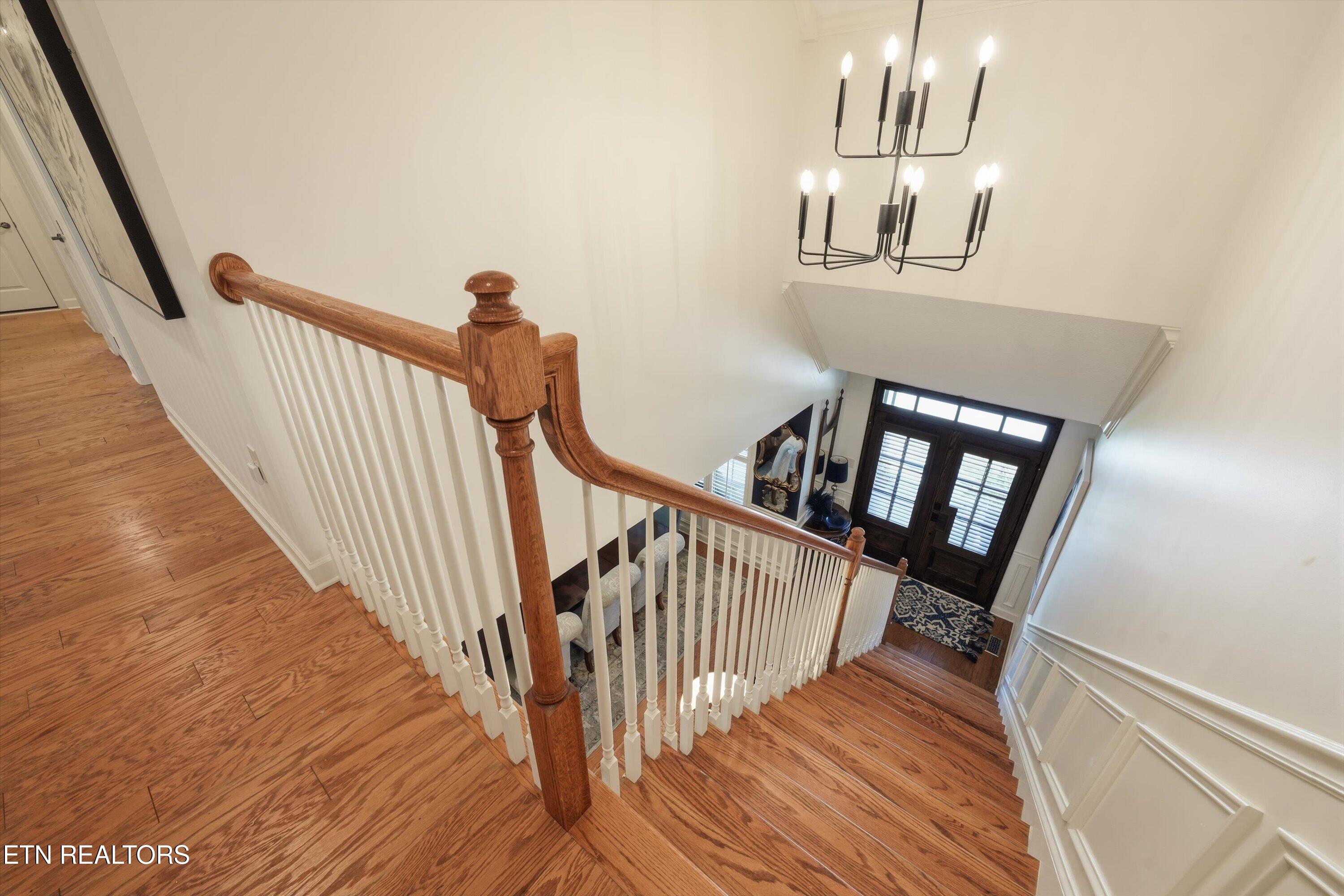 Hardwood staircase overlooking a foyer with a black entry door and chandelier.