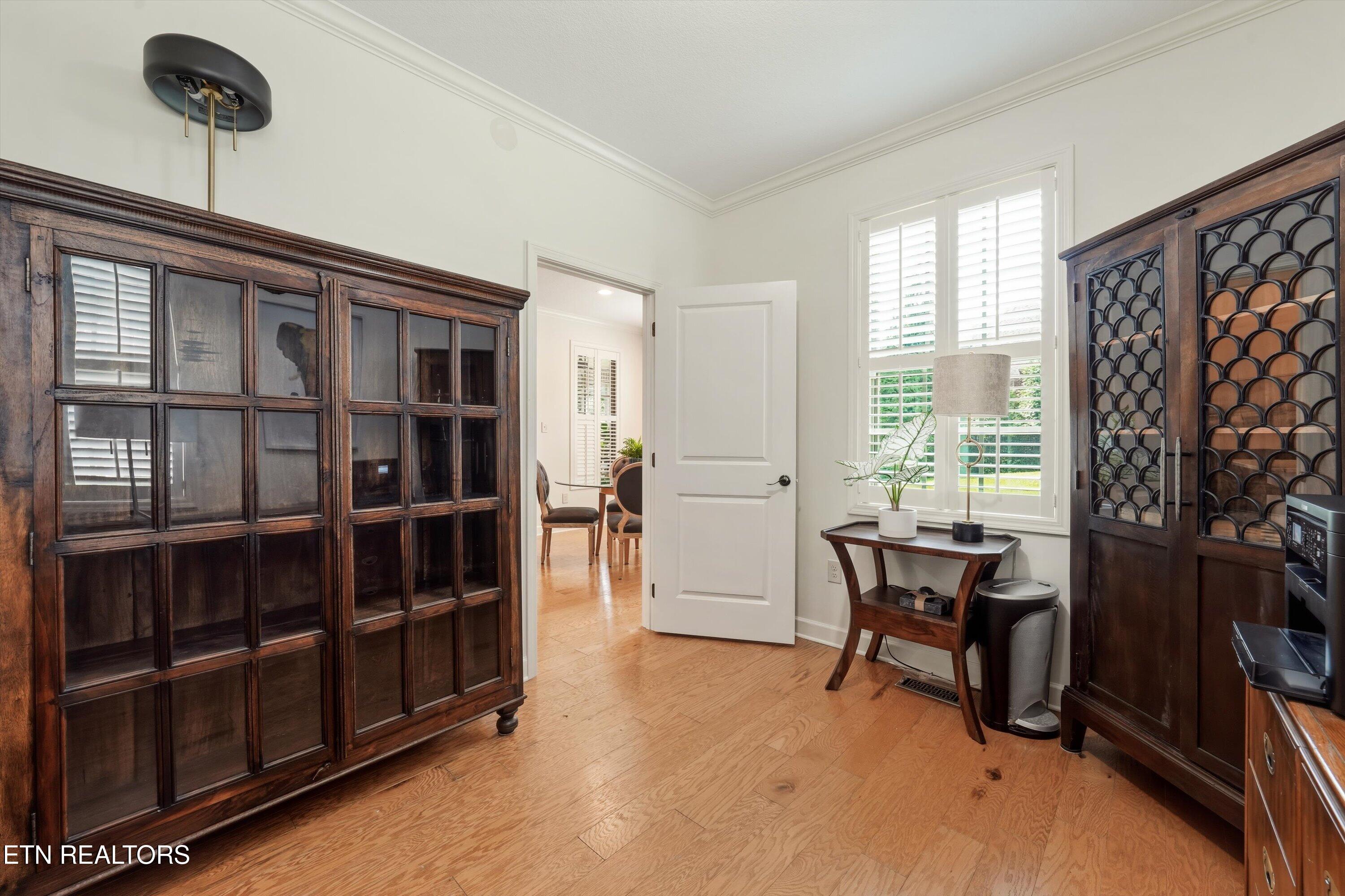 Room with hardwood floors, dark wood display cabinets, and shuttered windows beside an open doorway.