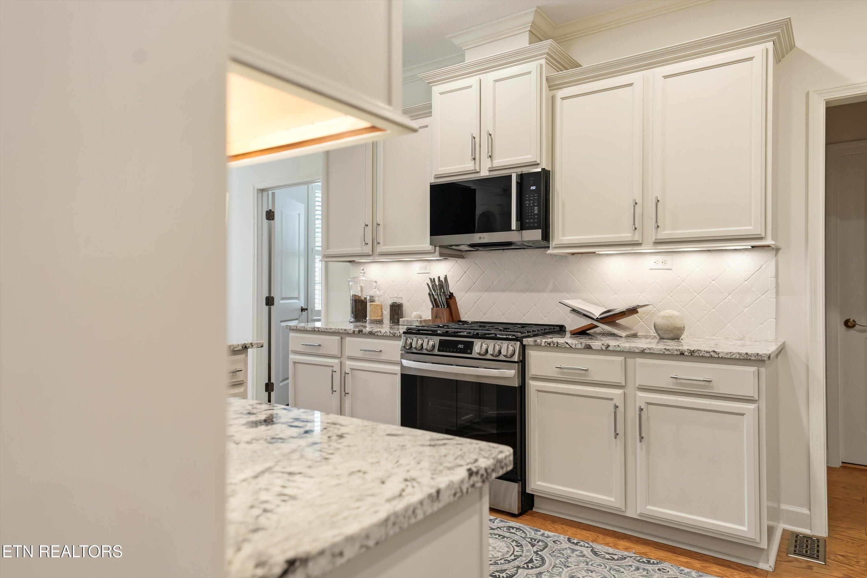 Kitchen with white cabinets, stainless steel range, granite counters, and a white tile backsplash.