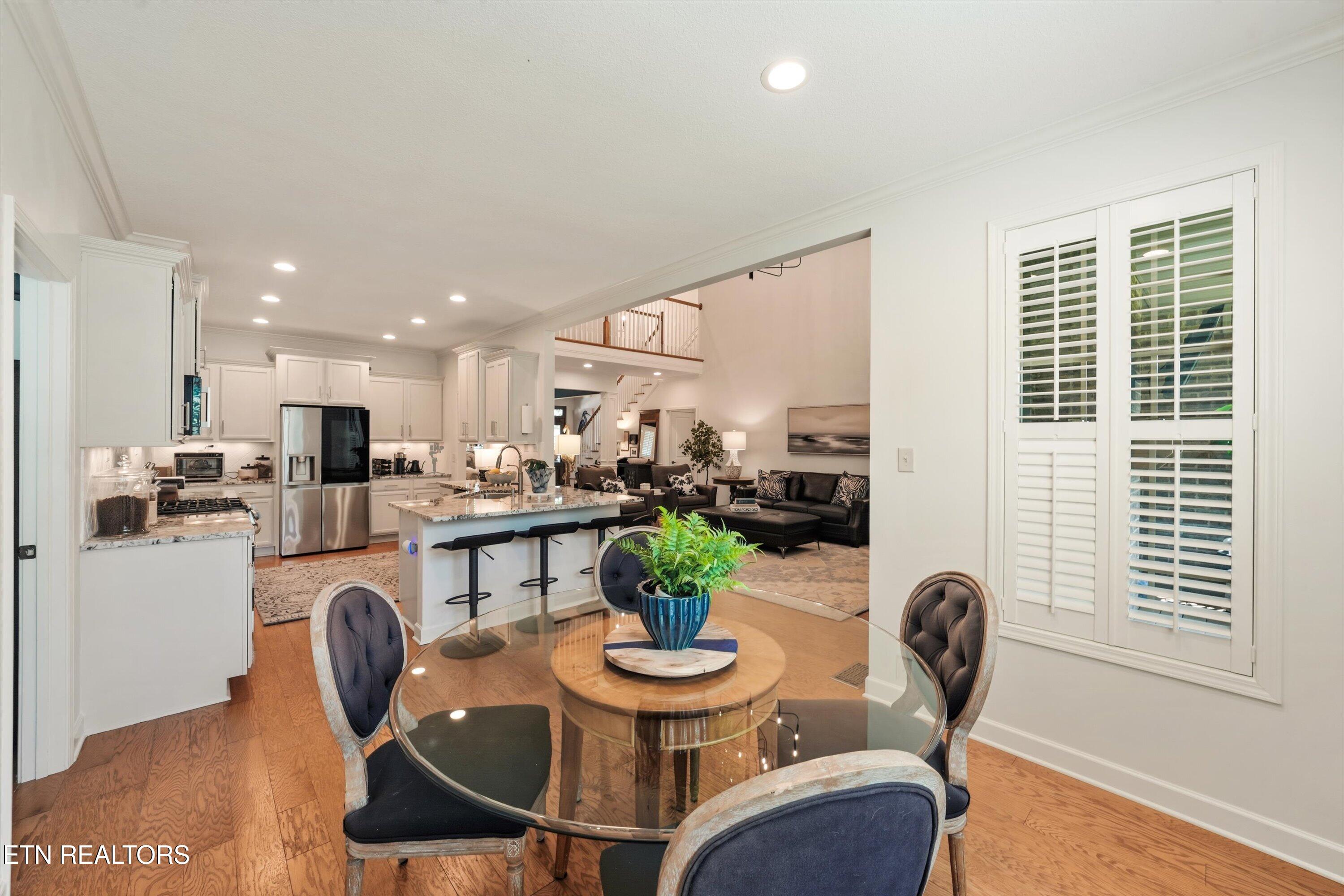 Open-plan kitchen and dining area with a granite island, glass table, and plantation shutters.