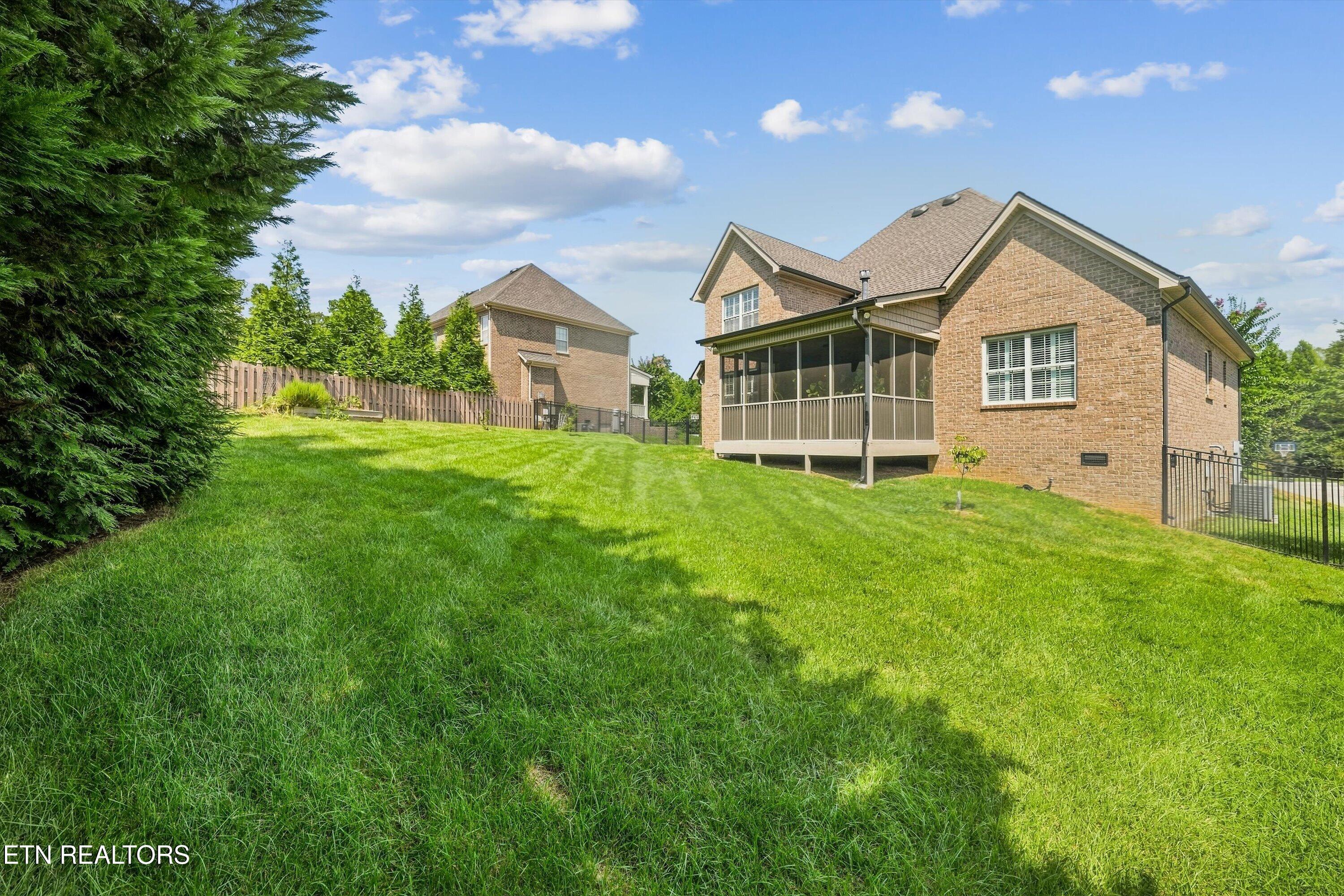 Brick home with a screened porch overlooking a broad, sloping lawn and fenced backyard.