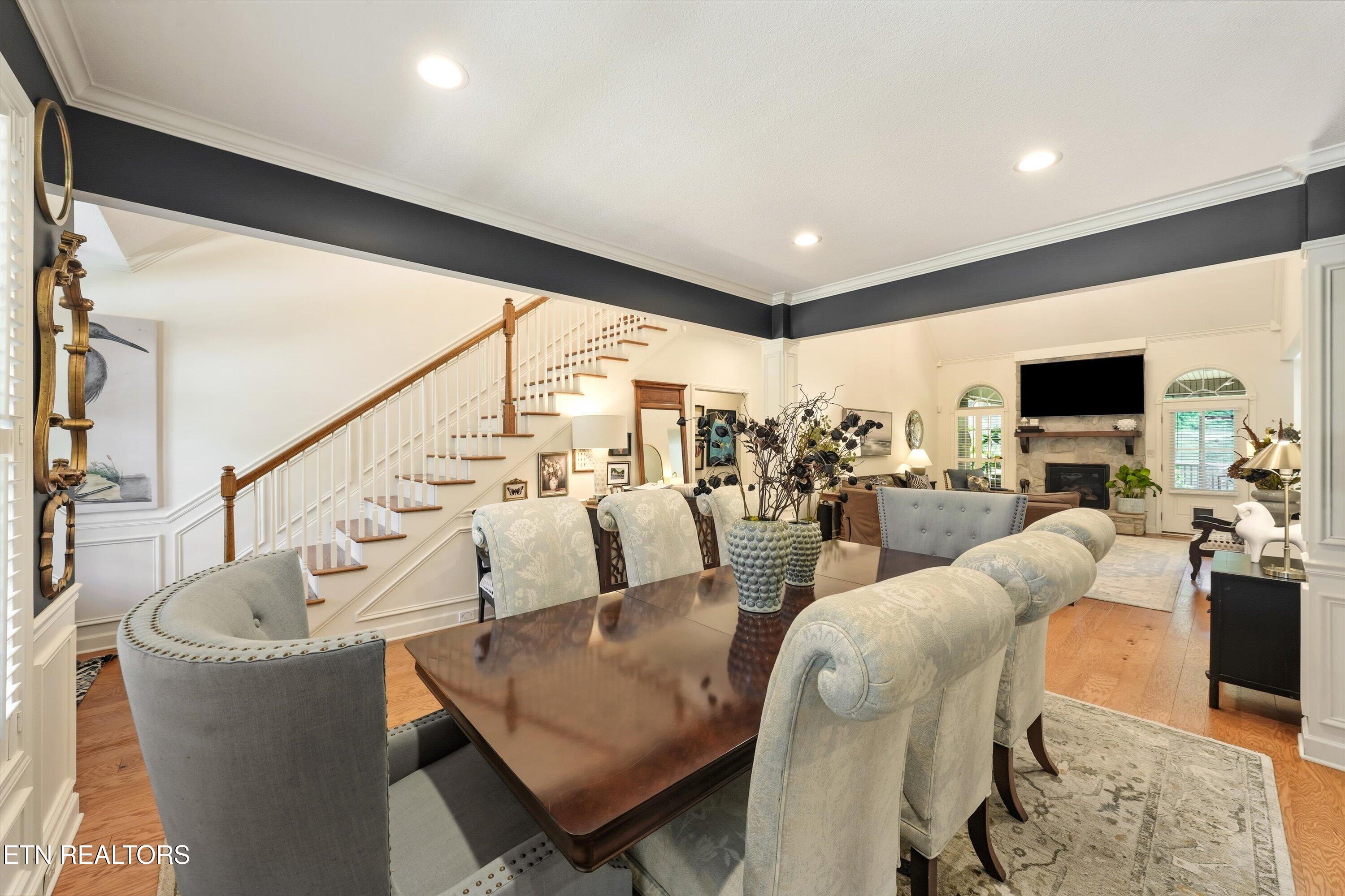 Open-plan dining and living room with a staircase, pale upholstered chairs, and stone fireplace.