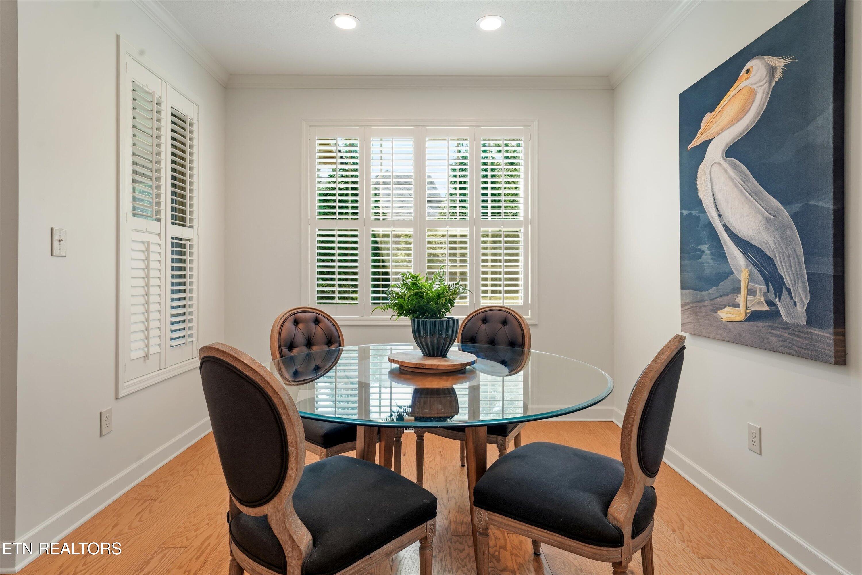 Dining room with a glass-top table, plantation shutters, hardwood floors, and large pelican artwork.