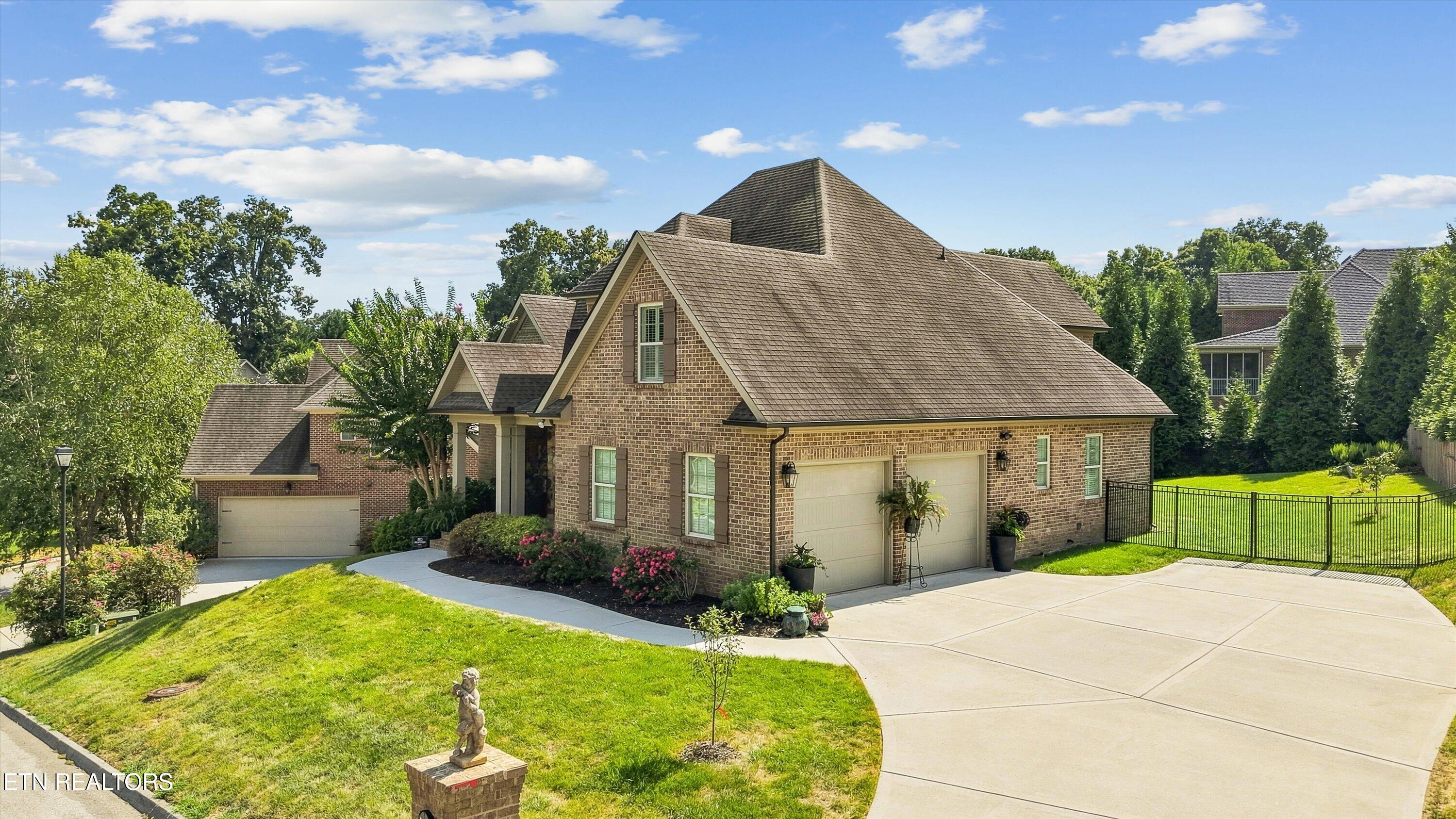 Brick home with steep gabled roof, two-car garage, broad driveway, and landscaped lawn.