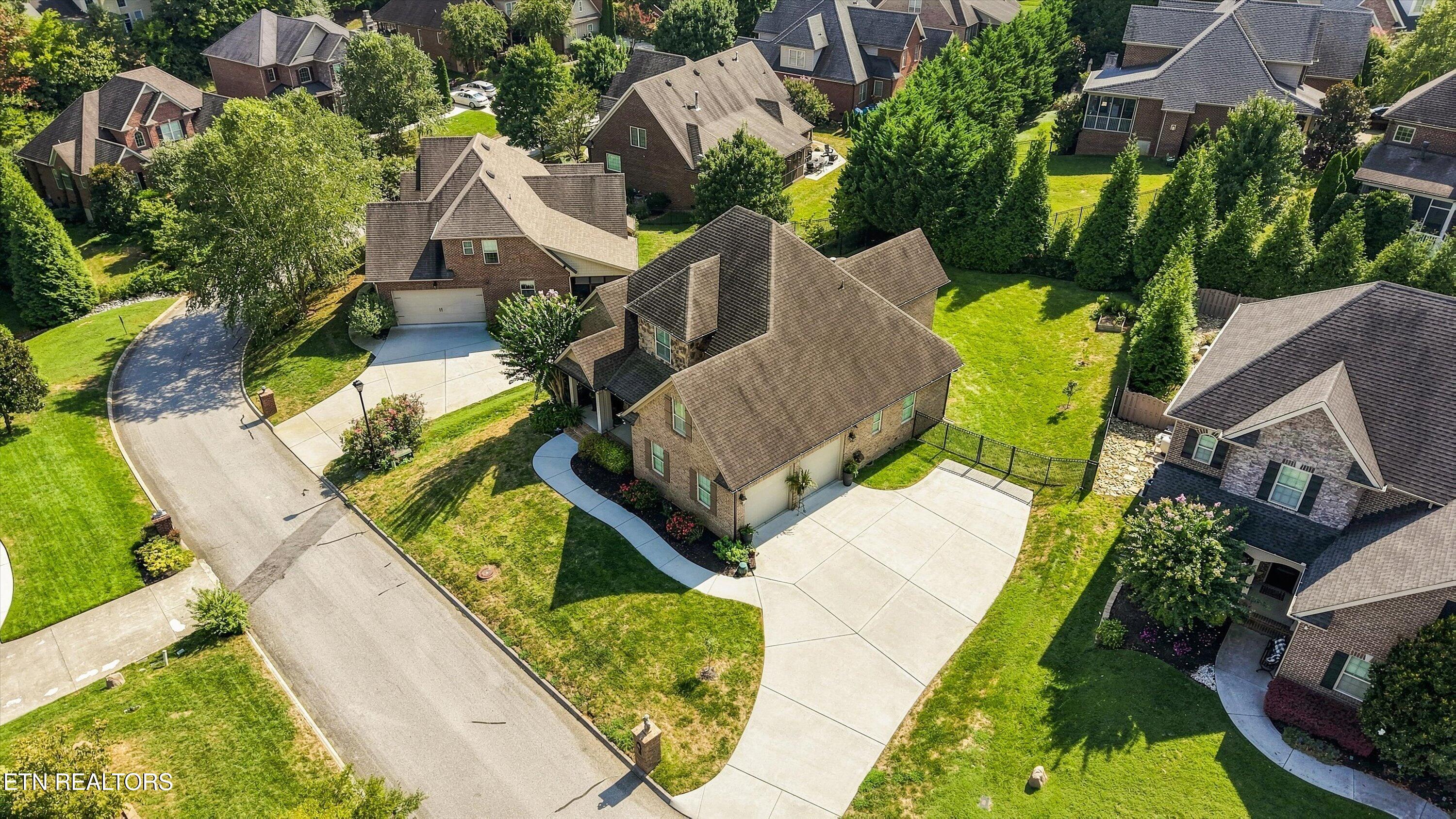Aerial view of a brick home with a broad driveway and landscaped lawn among neighboring houses.