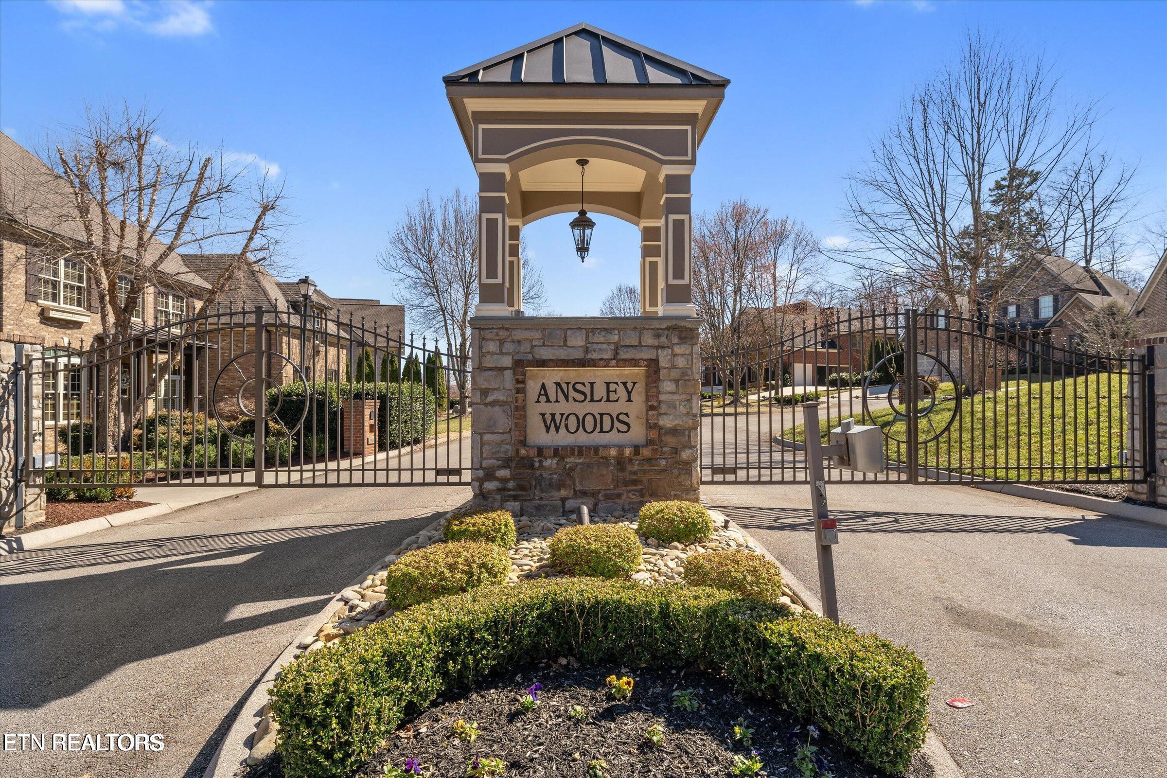 Ansley Woods gated entrance with a stone sign, wrought-iron gates, and landscaped shrubs.