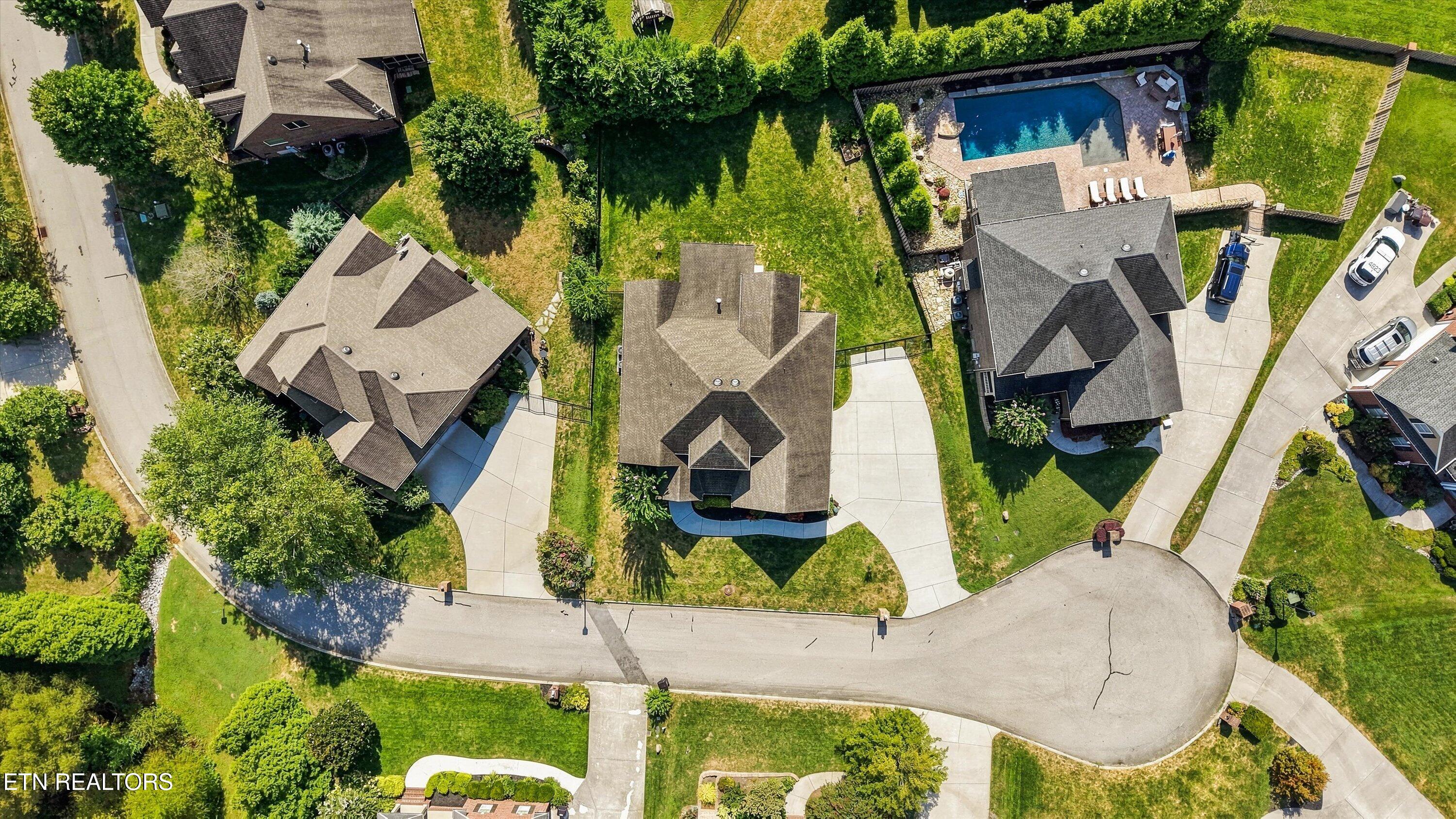 Aerial view of a house on a landscaped cul-de-sac, with neighboring homes and a backyard pool nearby.