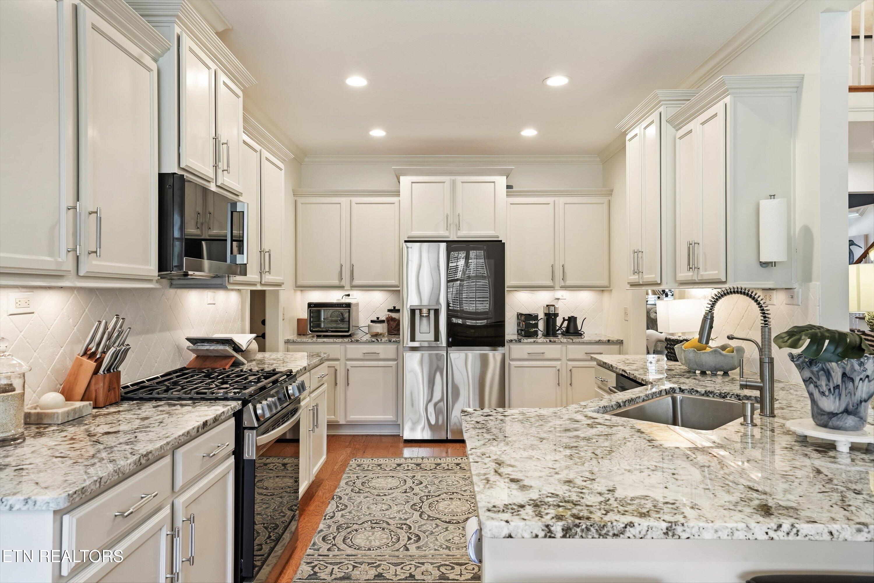 Kitchen with white cabinets, patterned granite counters, stainless appliances, and a large sink island.