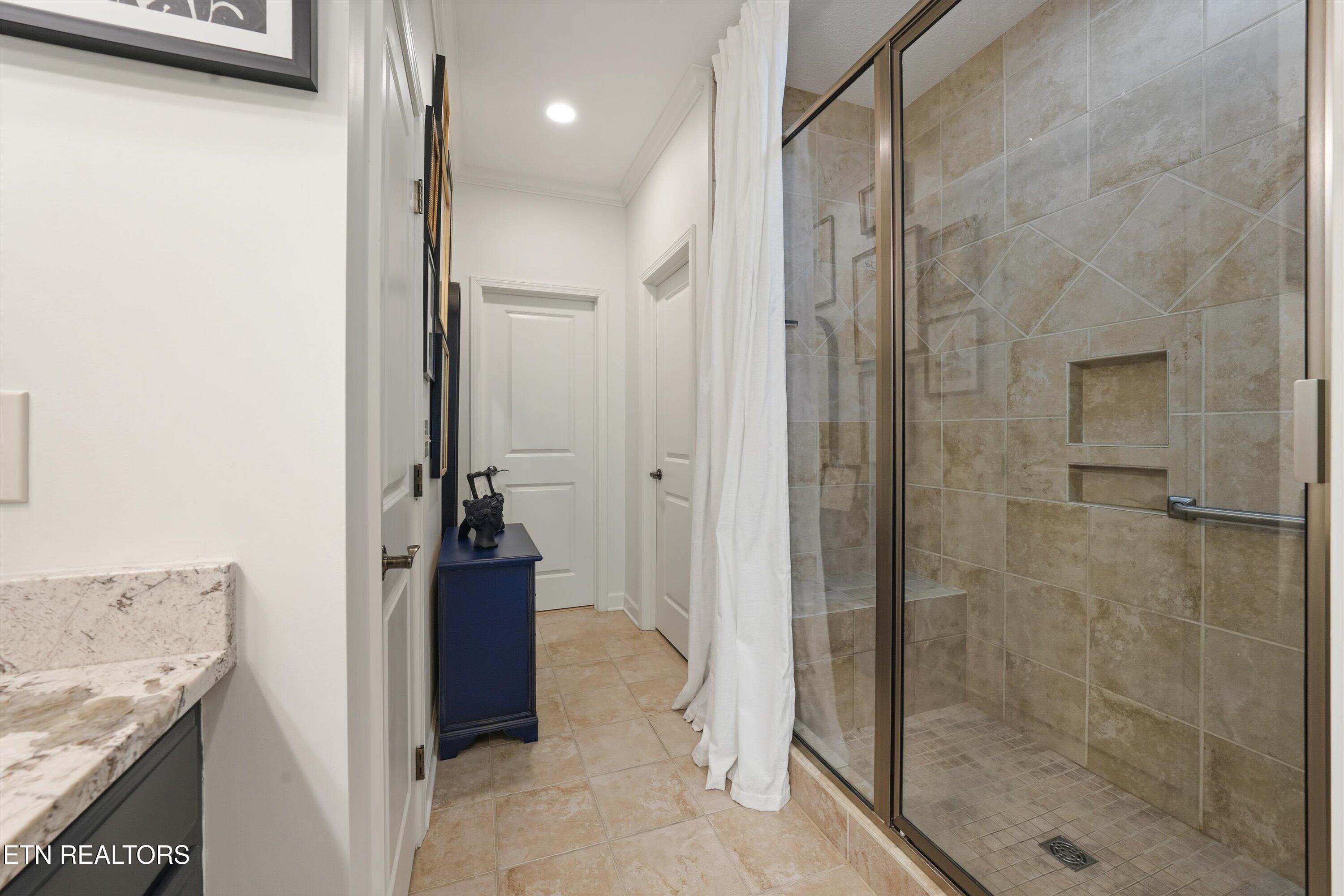 Bathroom with a glass-enclosed beige-tile shower, built-in bench, and granite vanity counter.
