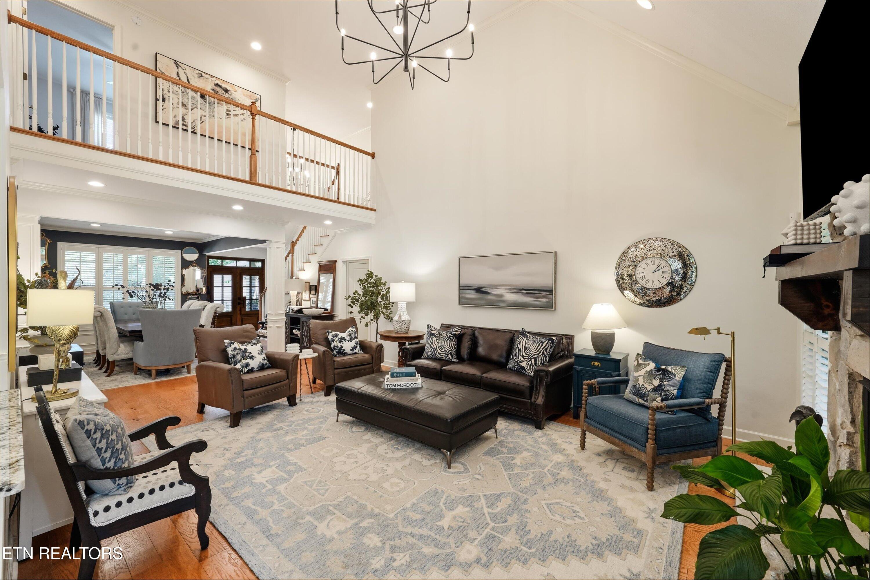 Two-story living room with leather seating, a stone fireplace, and an open upstairs railing.