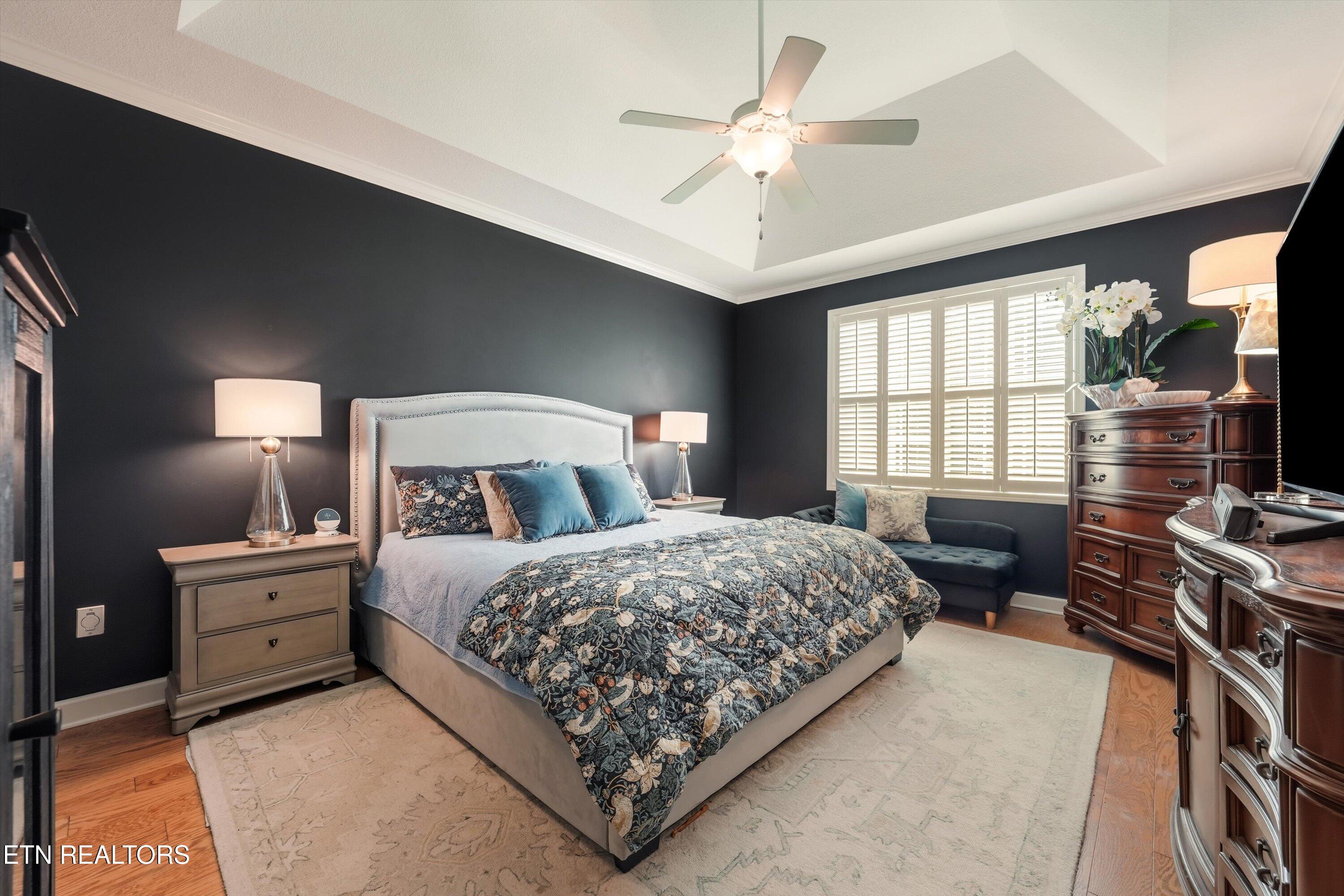 Furnished bedroom with a floral quilt, charcoal walls, shuttered window, and tray ceiling.