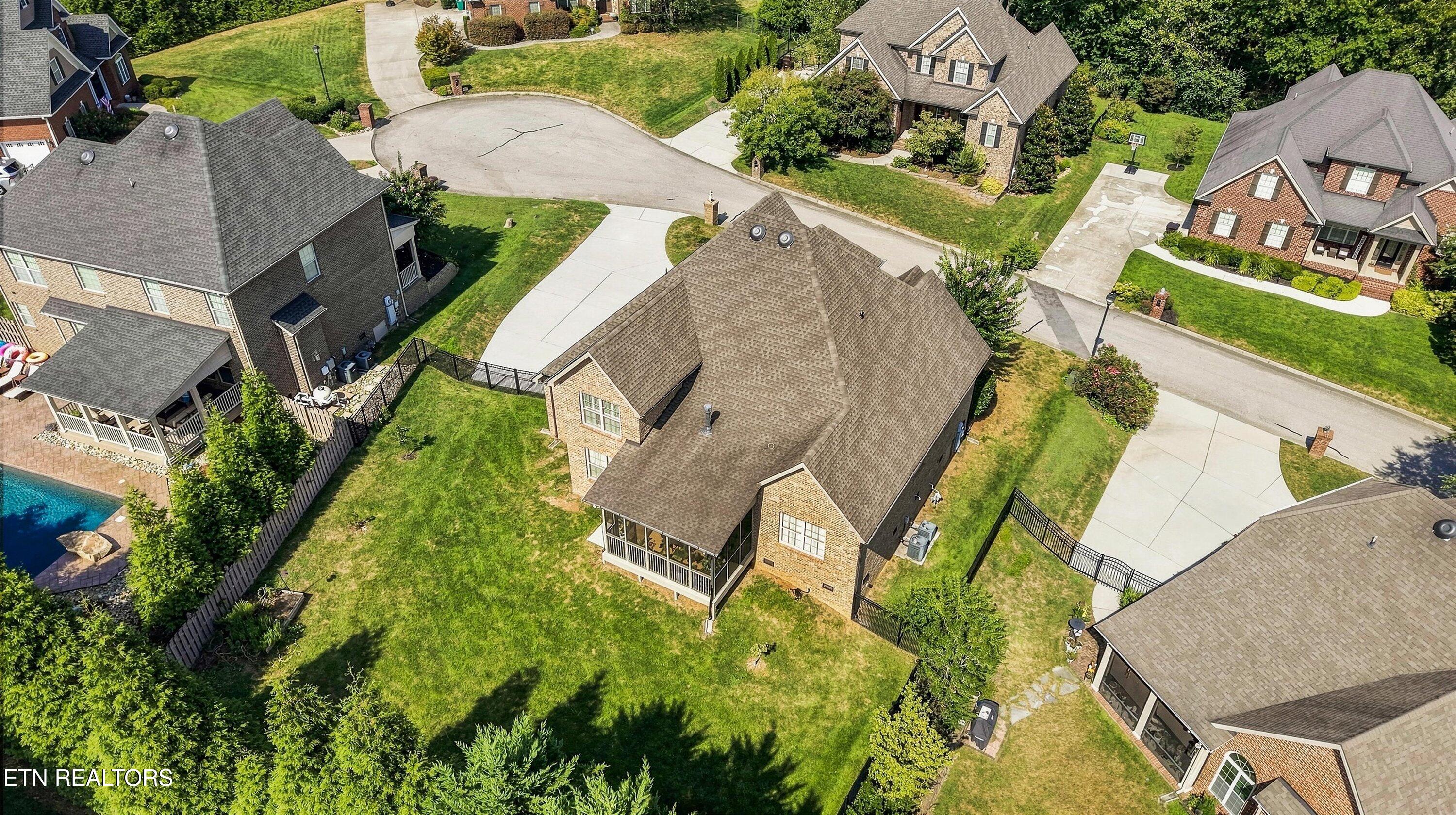 Aerial view of a brick home with a screened porch, large lawn, and neighboring homes.