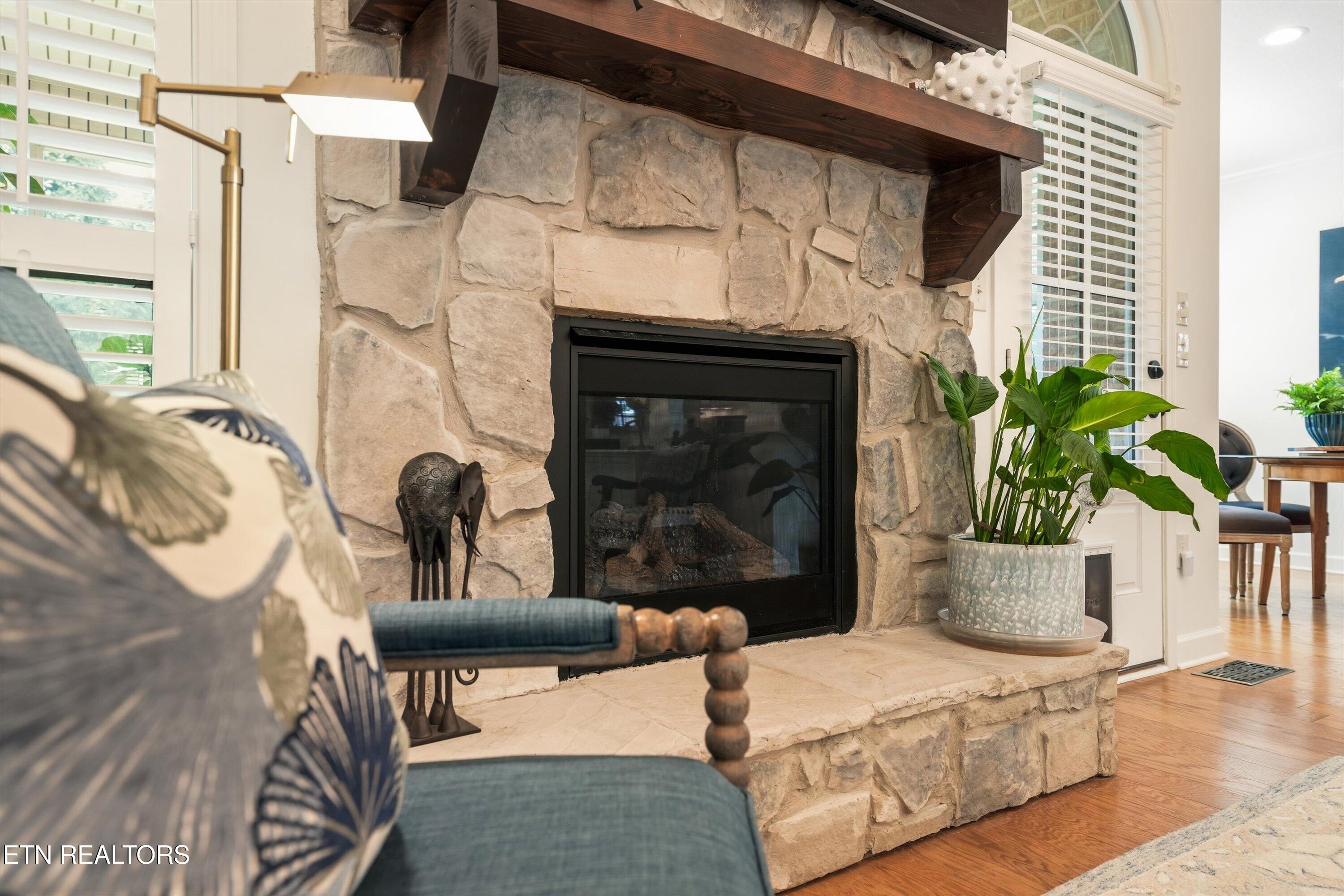 Stone fireplace with a dark wood mantel, blue chair, and potted plant in a bright living room.