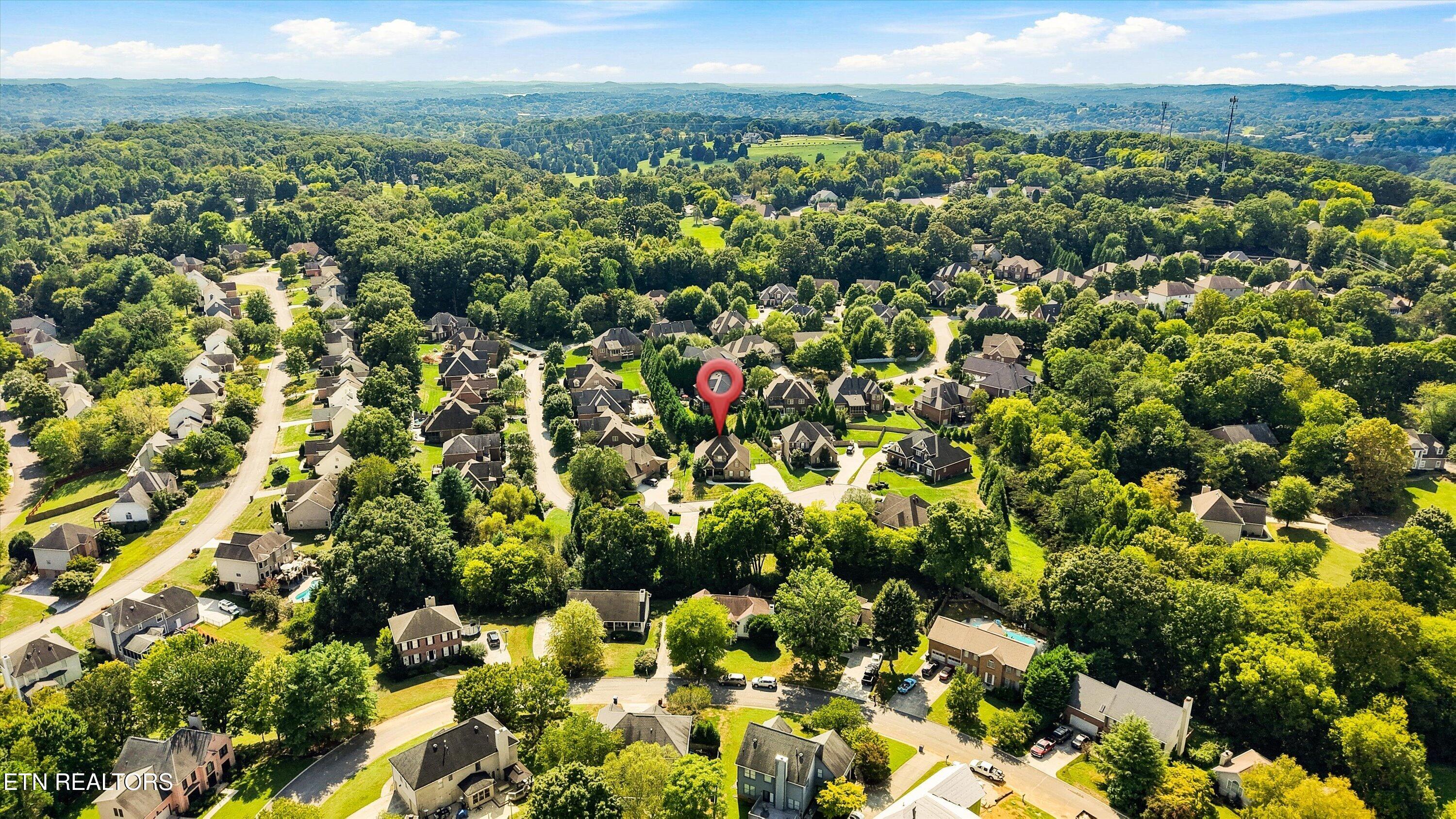 Aerial view of a wooded neighborhood, with a red map pin marking a home.