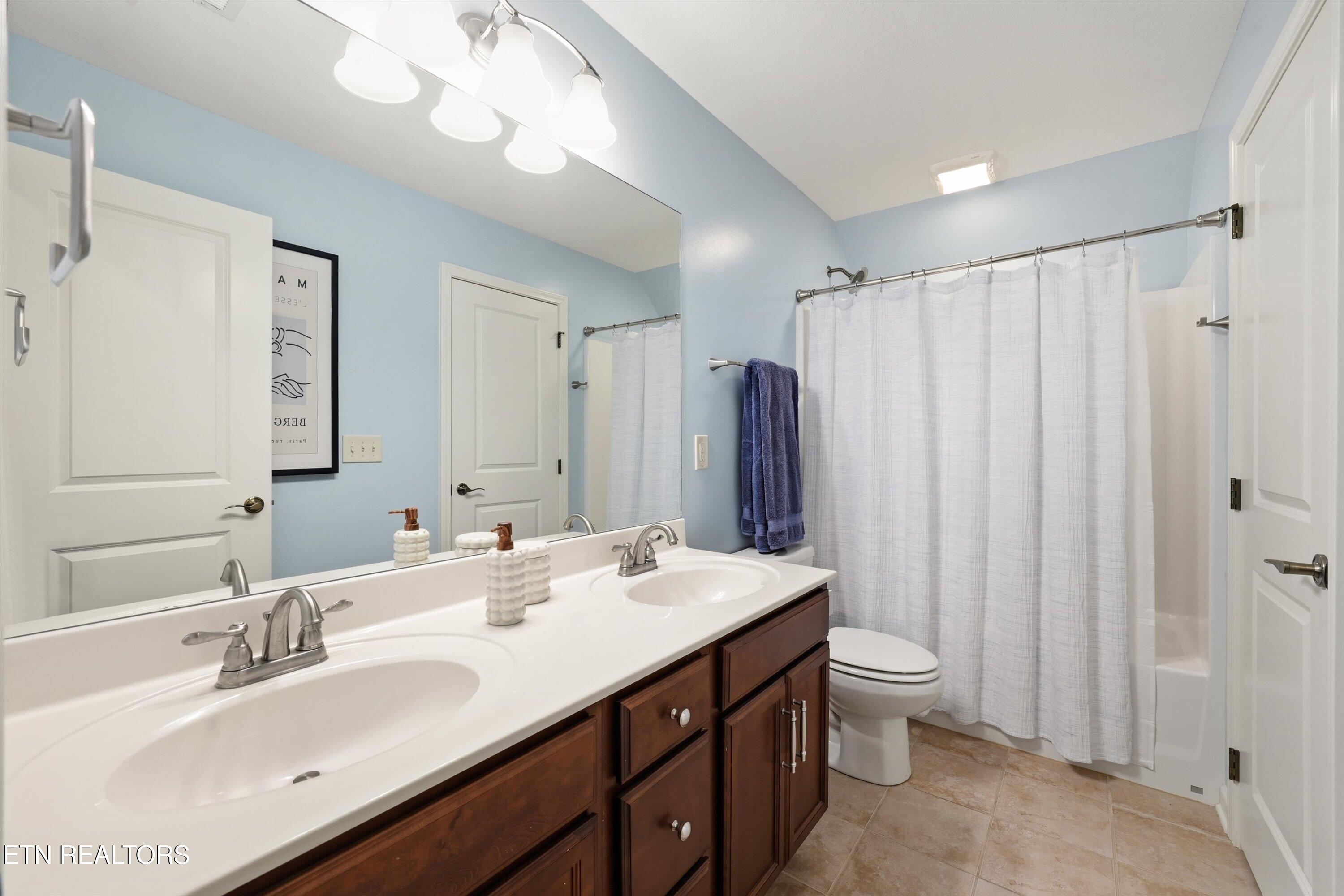 Bathroom with a double-sink dark wood vanity, light blue walls, and a white shower curtain.