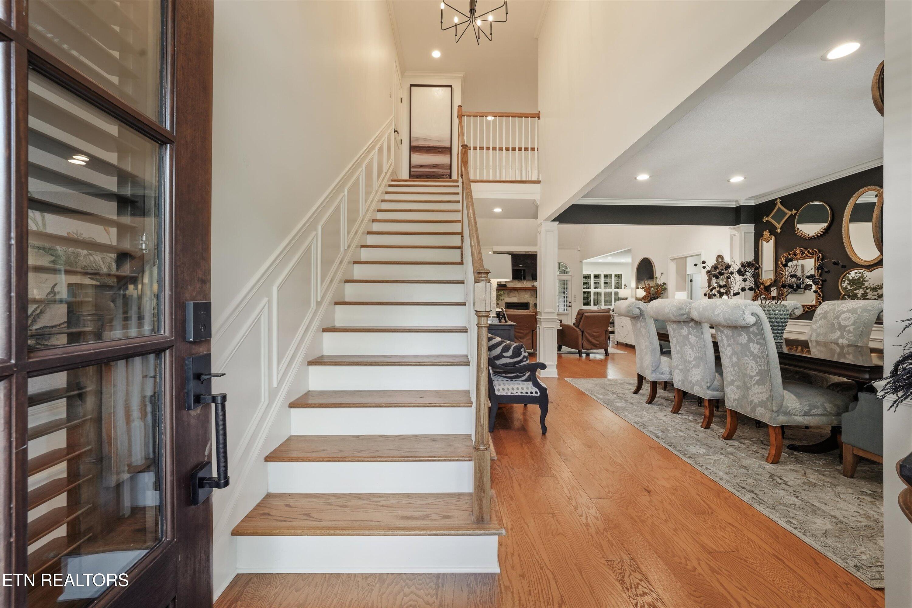 Entryway staircase beside a dining room with upholstered chairs and decorative mirrors.