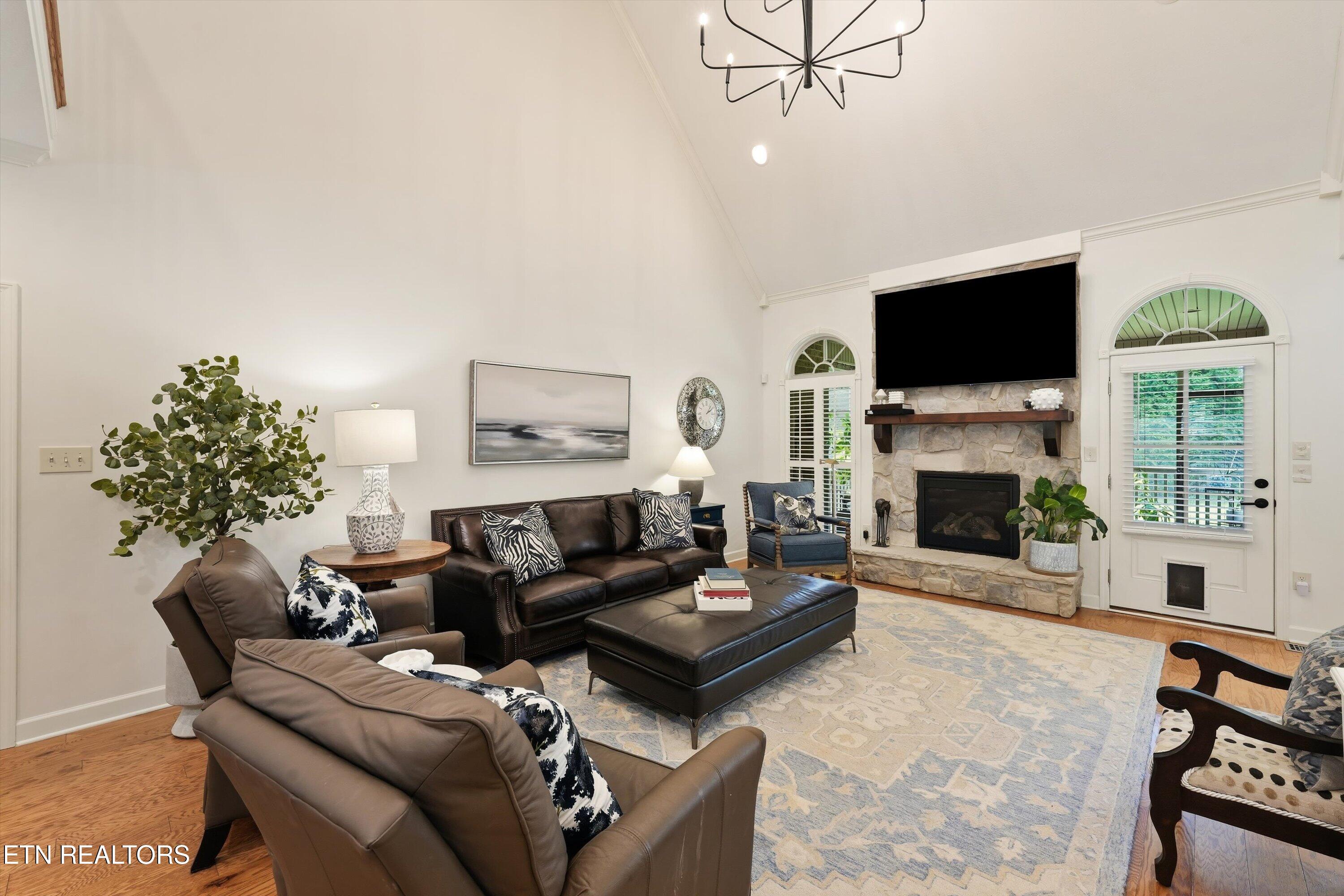 Furnished living room with a vaulted ceiling, stone fireplace, and leather seating.
