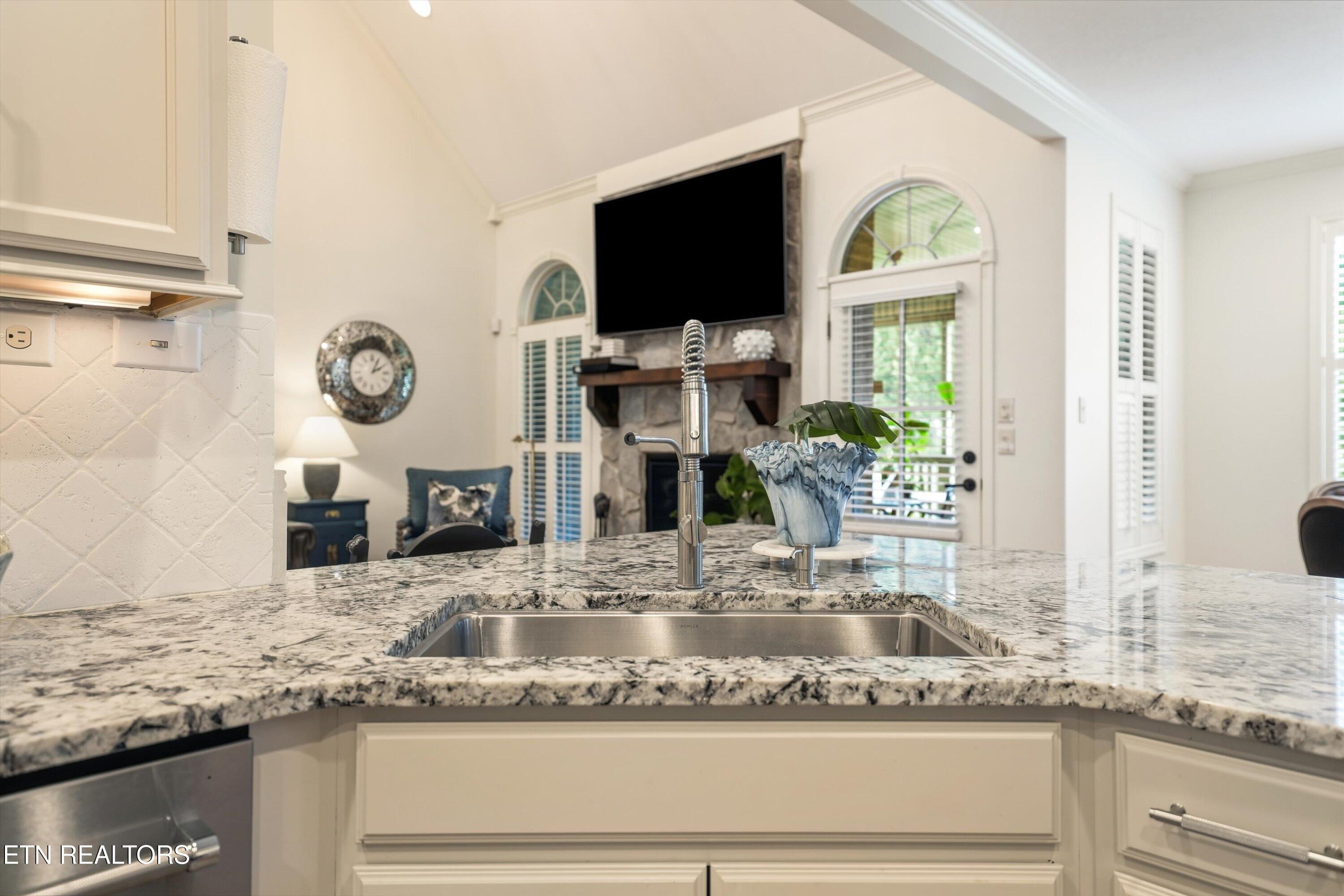 Kitchen with granite island and sink overlooking a living room with a stone fireplace.