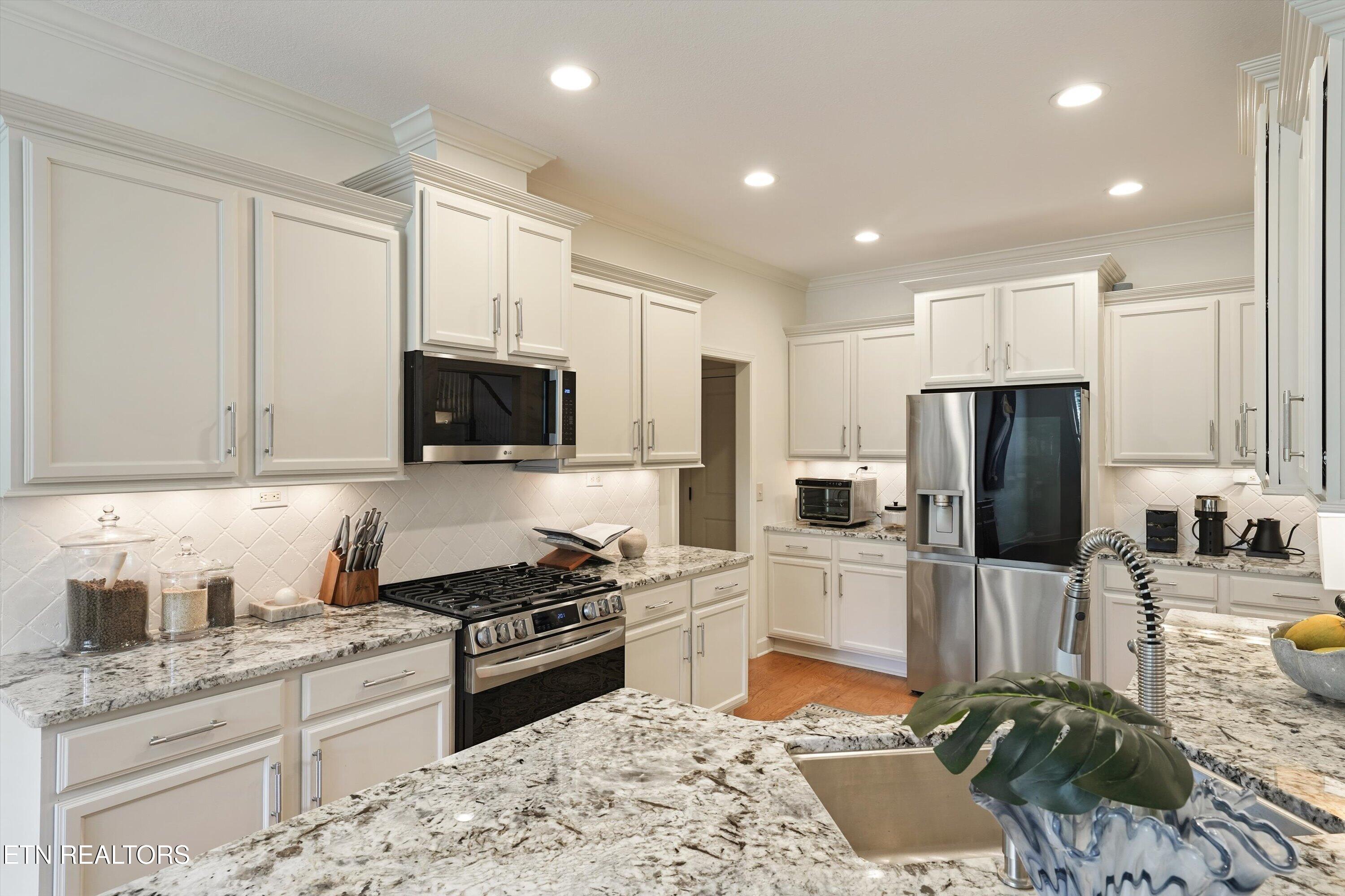 Kitchen with white cabinets, granite countertops, stainless-steel appliances, and a large island sink.