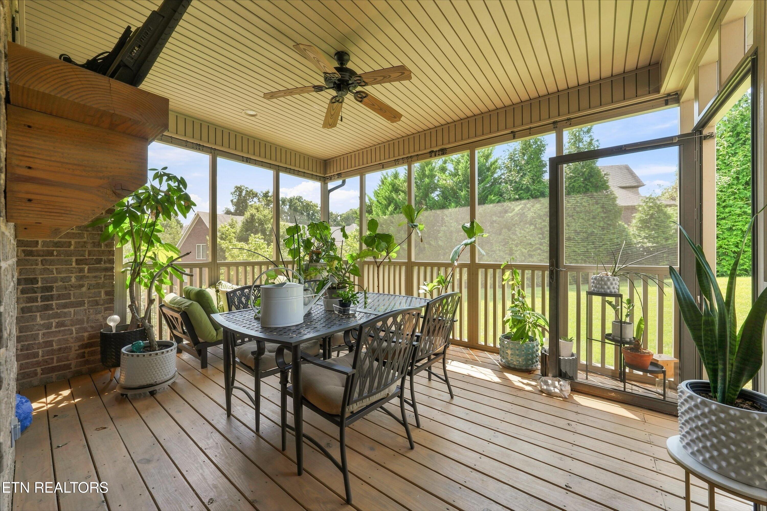 Screened-in porch with a dining set, ceiling fan, and potted plants overlooking the lawn.