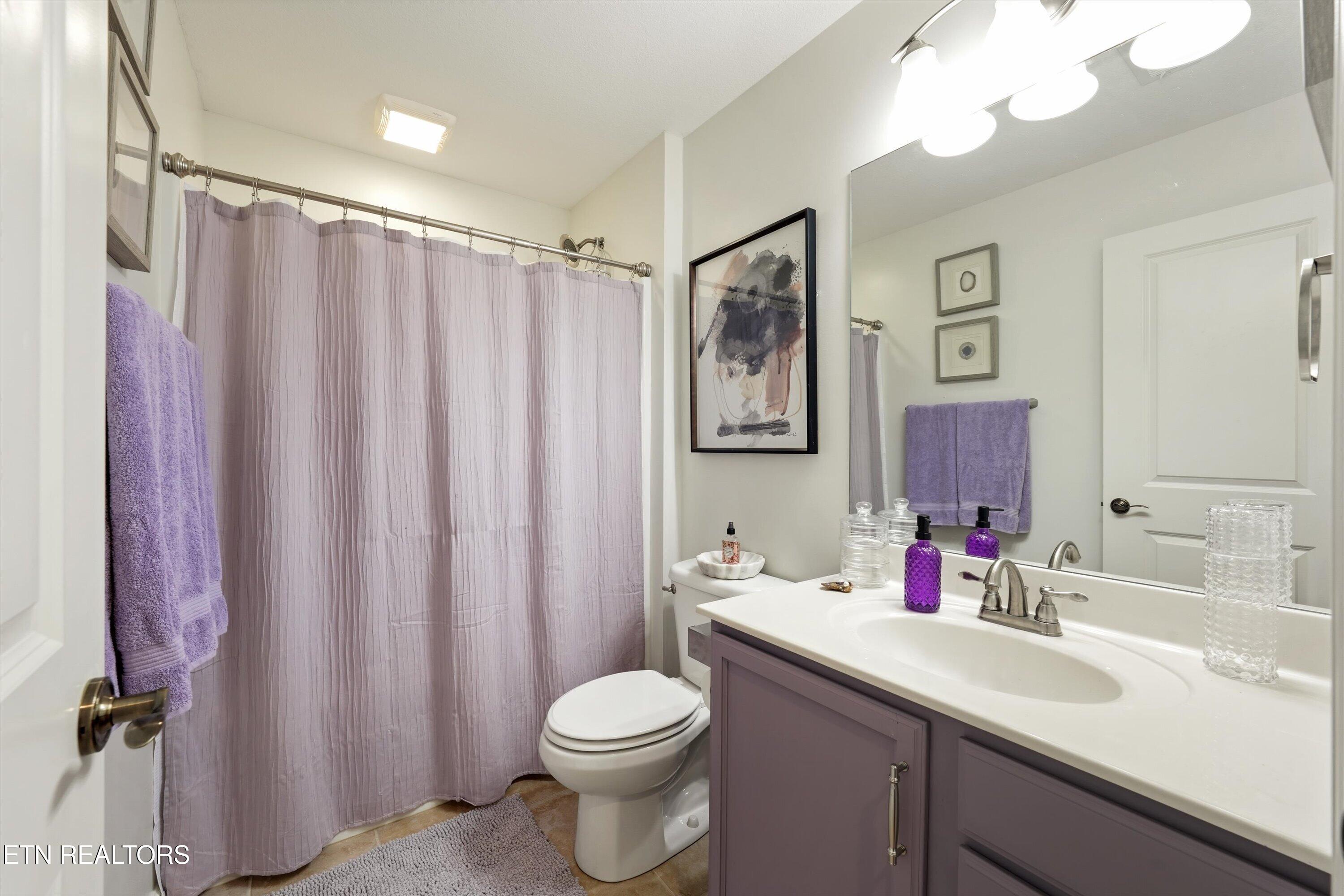 Bathroom with a lavender shower curtain and towels, toilet, and mauve vanity.