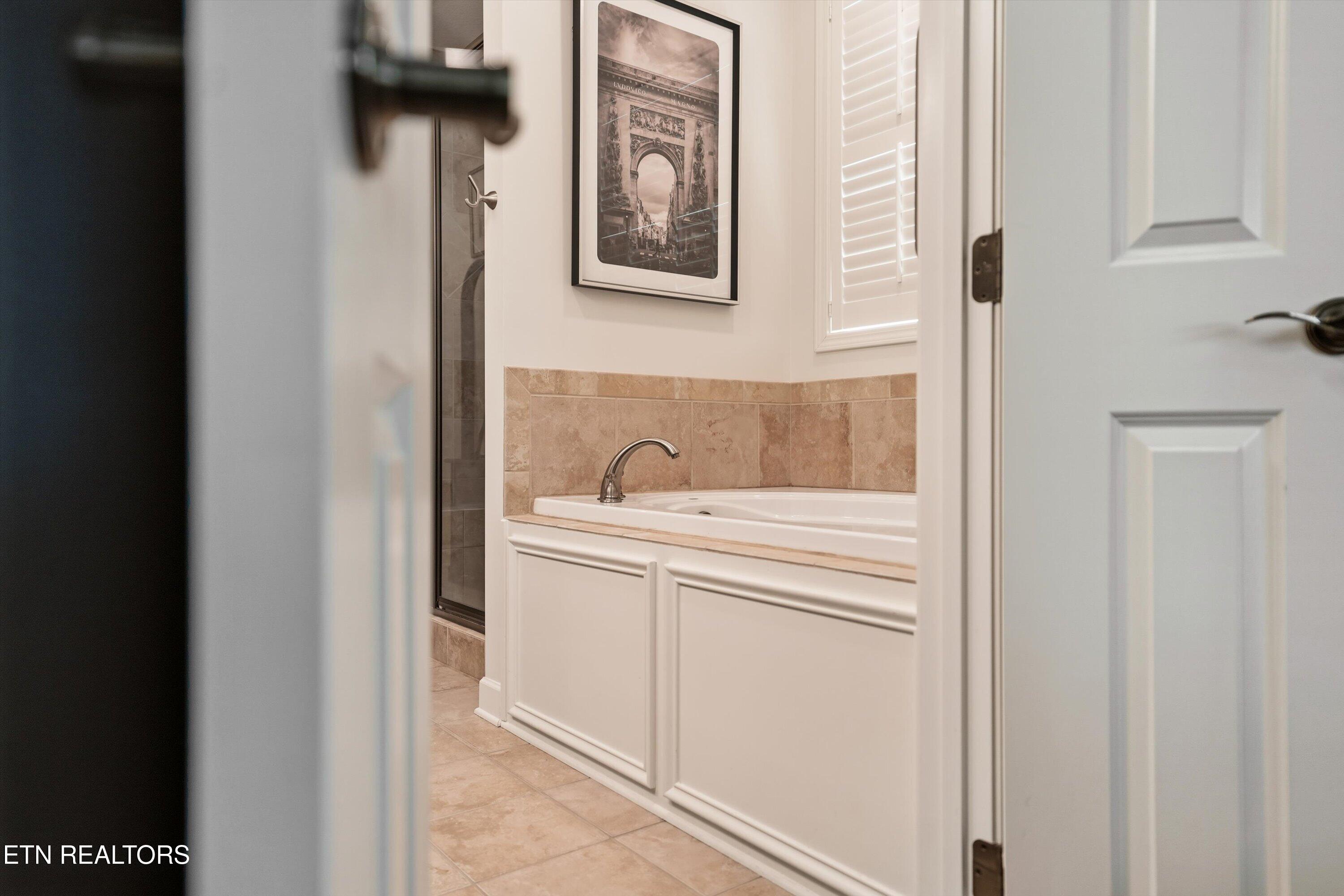Bathroom with a white soaking tub, tan tile surround, and glass shower enclosure.