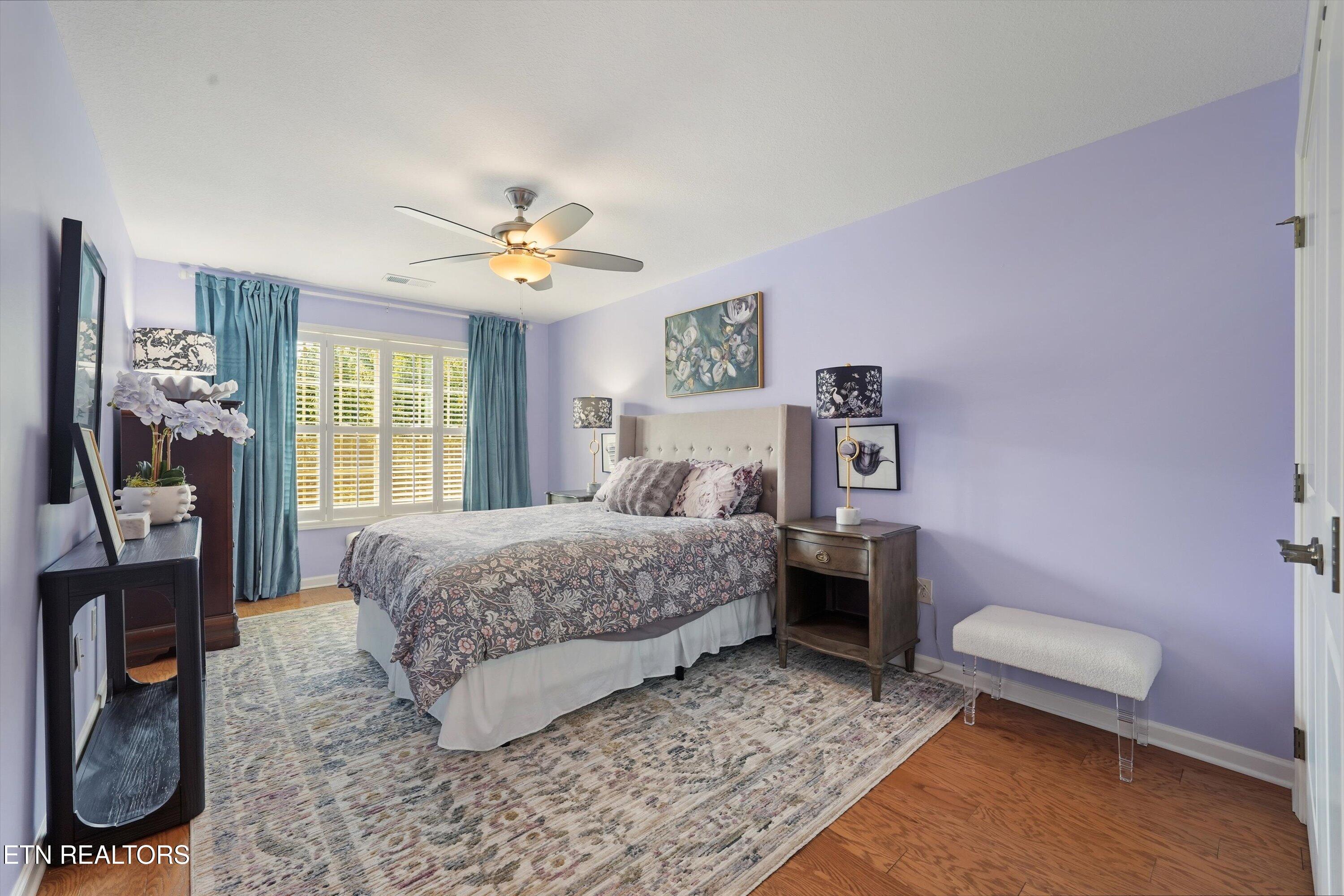 Bedroom with lavender walls, a floral bedspread, teal curtains, and plantation shutters.