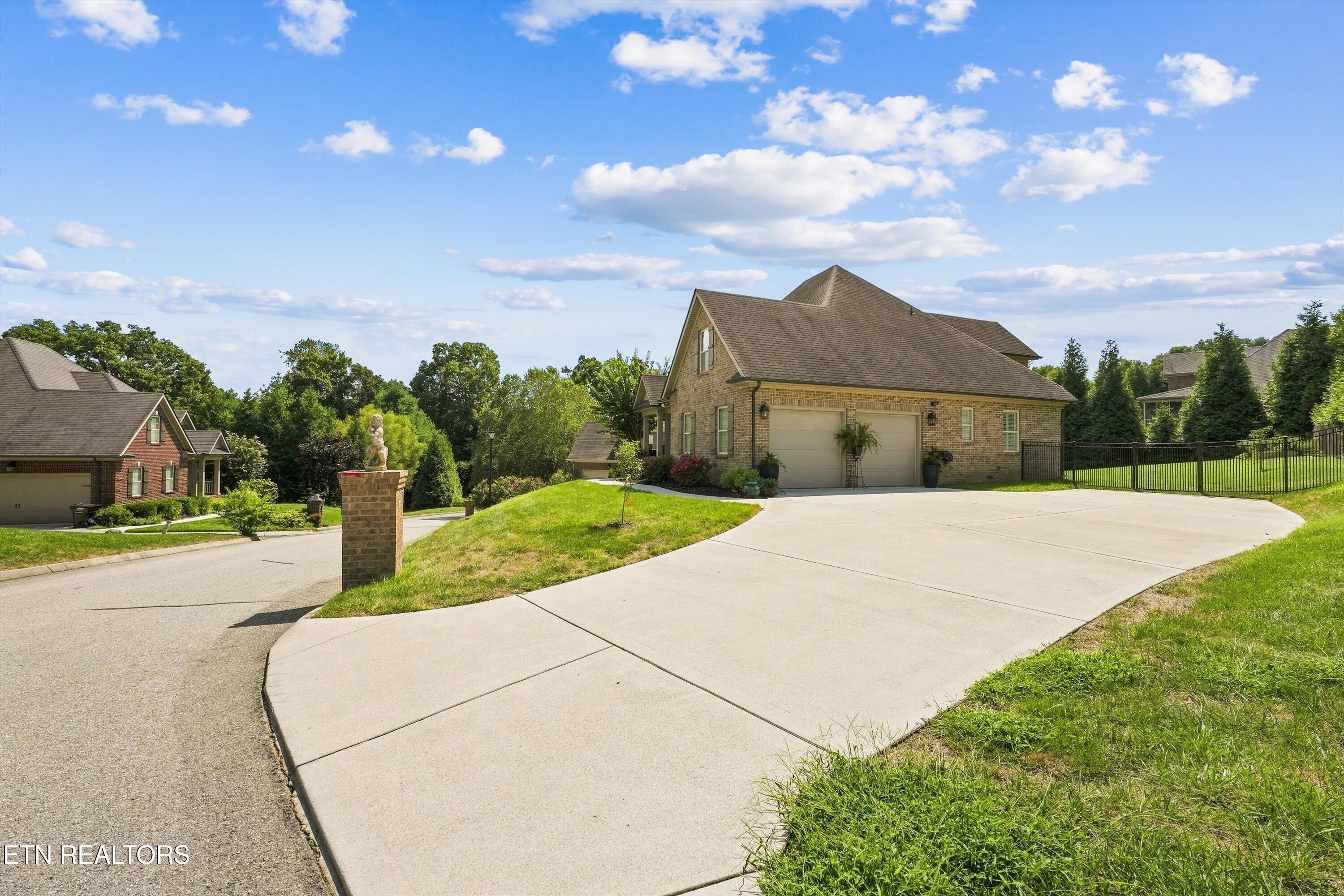 Brick home with a two-car garage, broad curved driveway, and black metal fence.