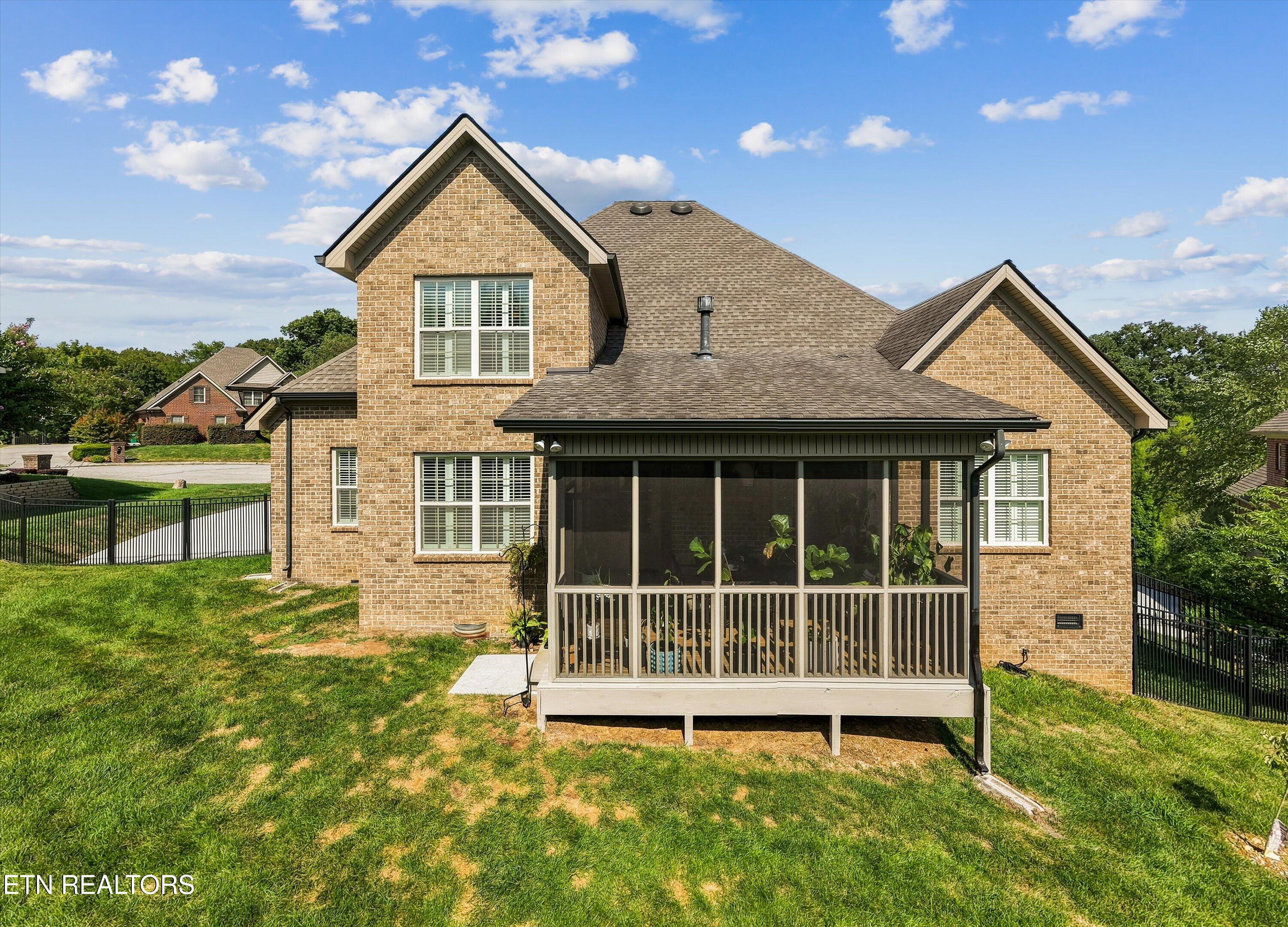 Rear of a two-story brick home with a large screened porch and fenced lawn.
