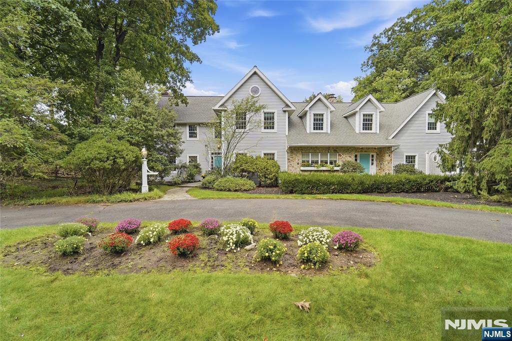 Gray-sided home with stone accents, multiple gables, and a colorful flower bed in front.