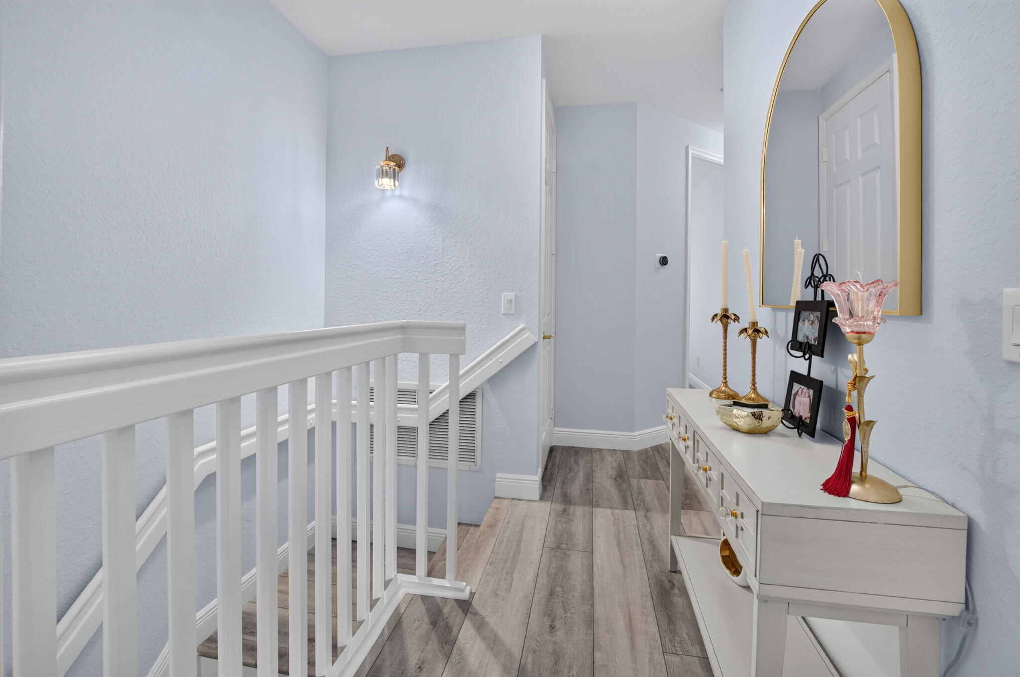 Upstairs hallway with a white stair railing, gray tile flooring, and a console beneath a gold-framed mirror.