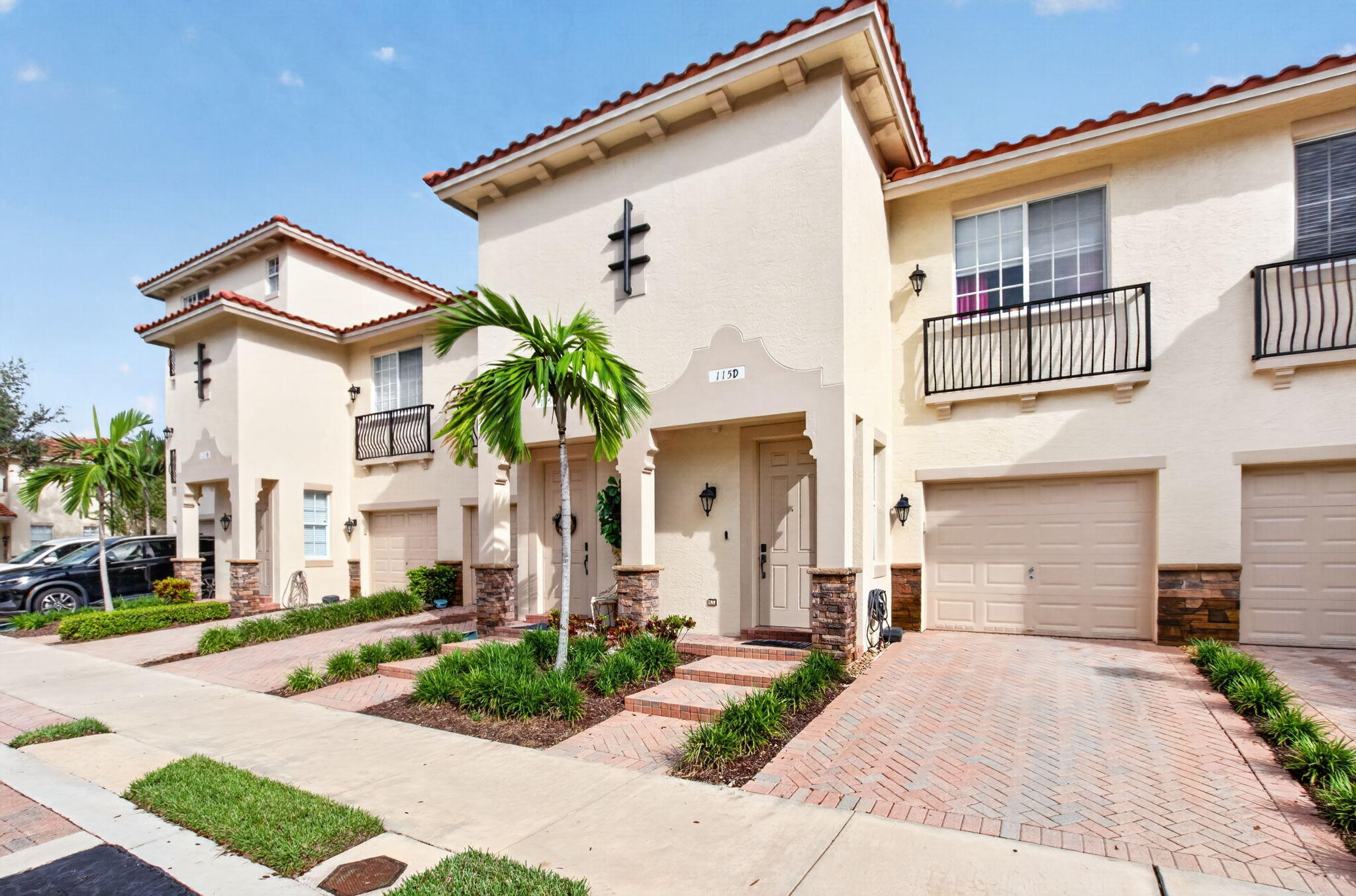 Townhouse exterior with red tile roof, black balconies, brick driveway, and palm-landscaped entrance.