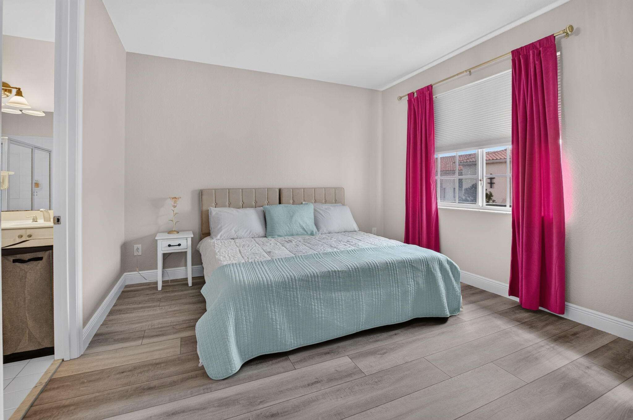 Bedroom with pale blue bedding, magenta curtains, and a bathroom doorway.