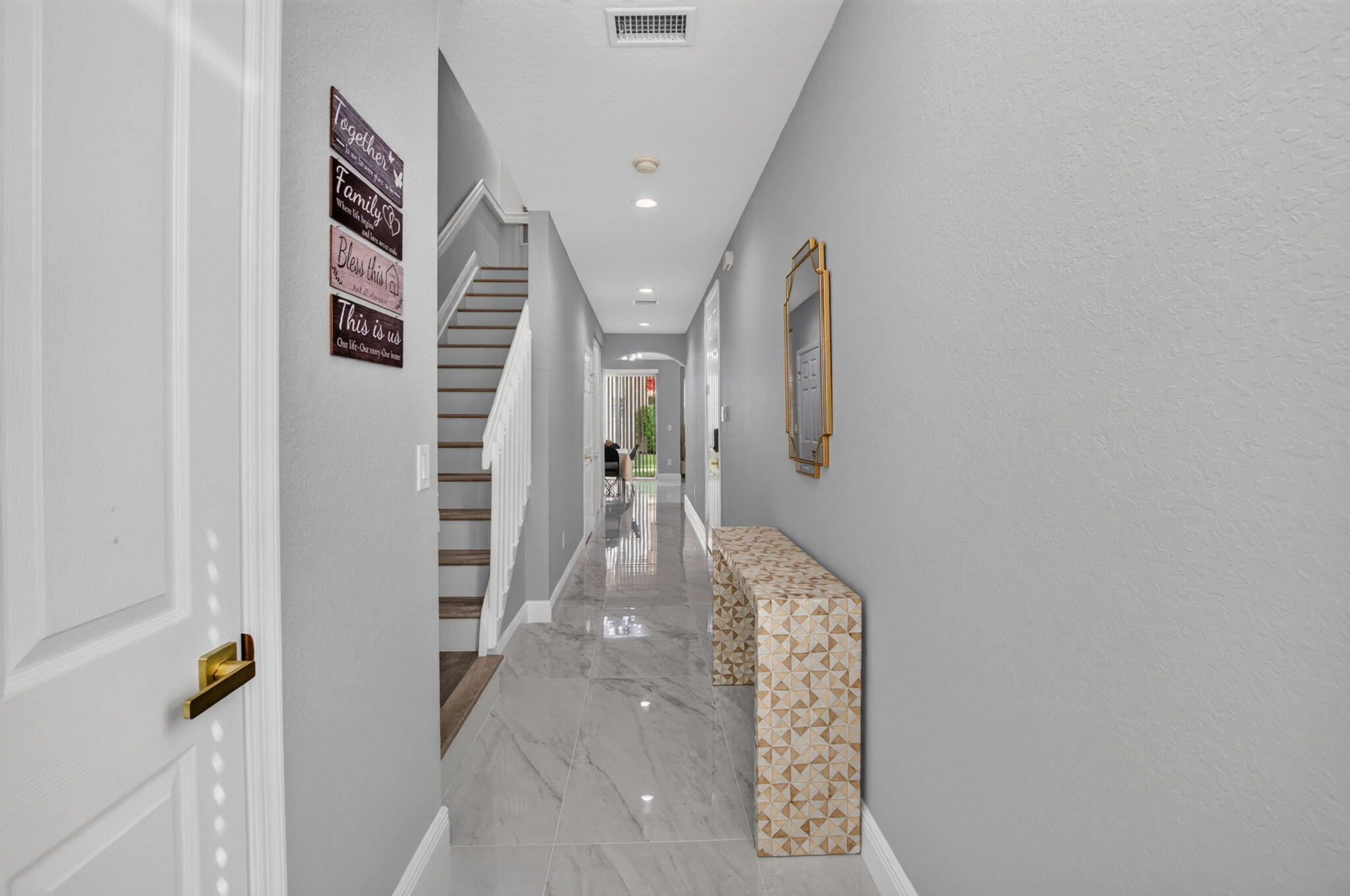 Bright hallway with glossy tile floors, a wood-tread staircase, and a patterned console bench.