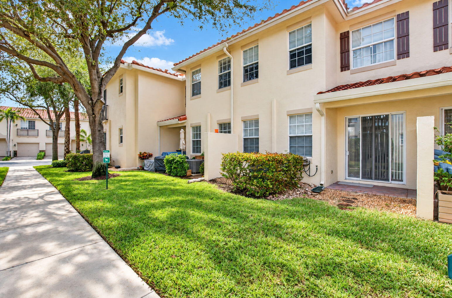 Two-story townhouse with terracotta roof tiles, dark shutters, and a landscaped lawn.