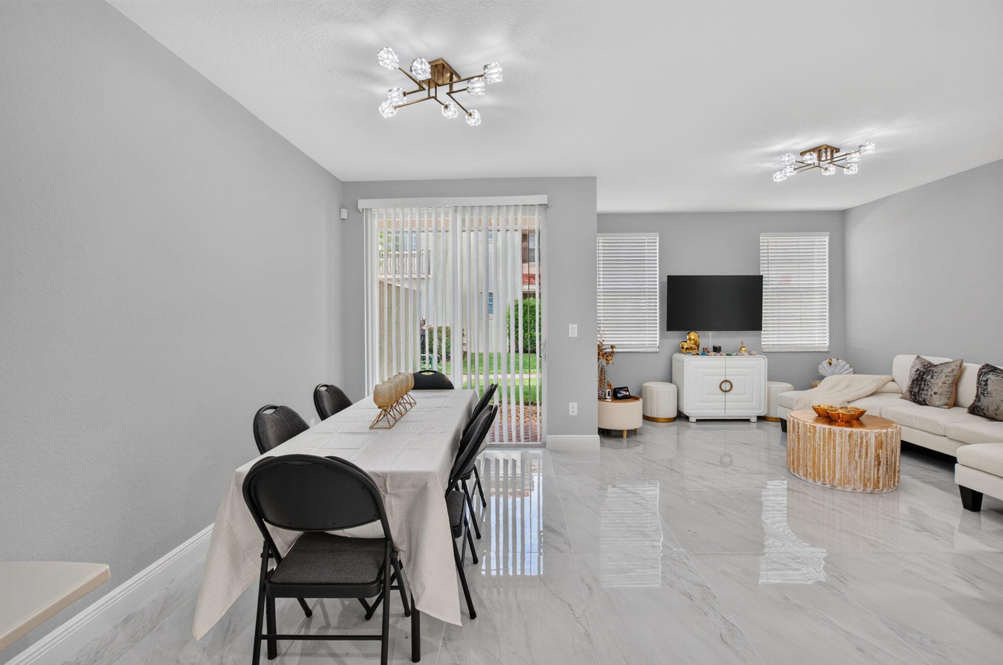 Open-plan living and dining room with glossy tile floors, a white sectional, and sliding glass doors.