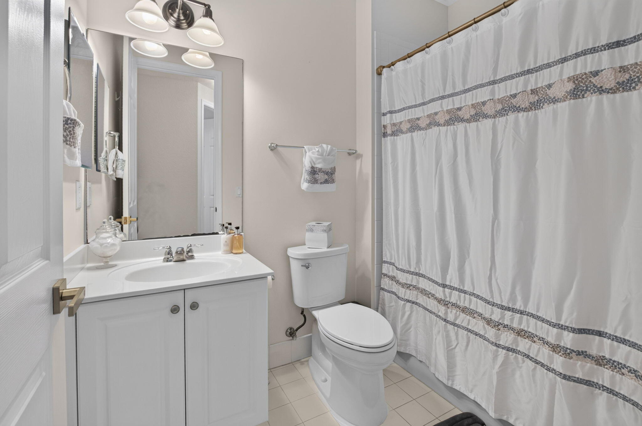 Bathroom with a white vanity and sink, toilet, and patterned white shower curtain.