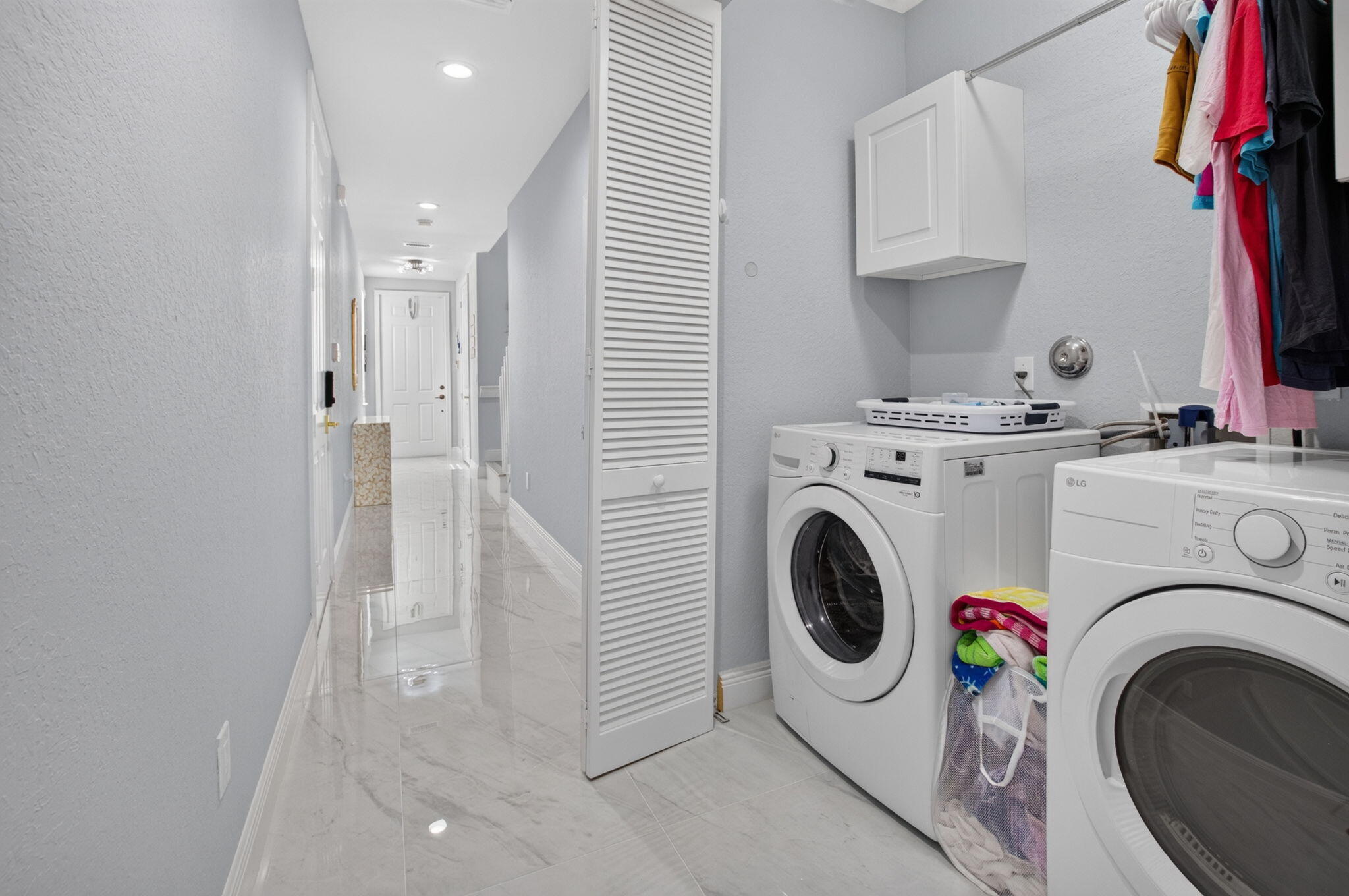 Laundry room with front-loading washer and dryer beside a bright tiled hallway.