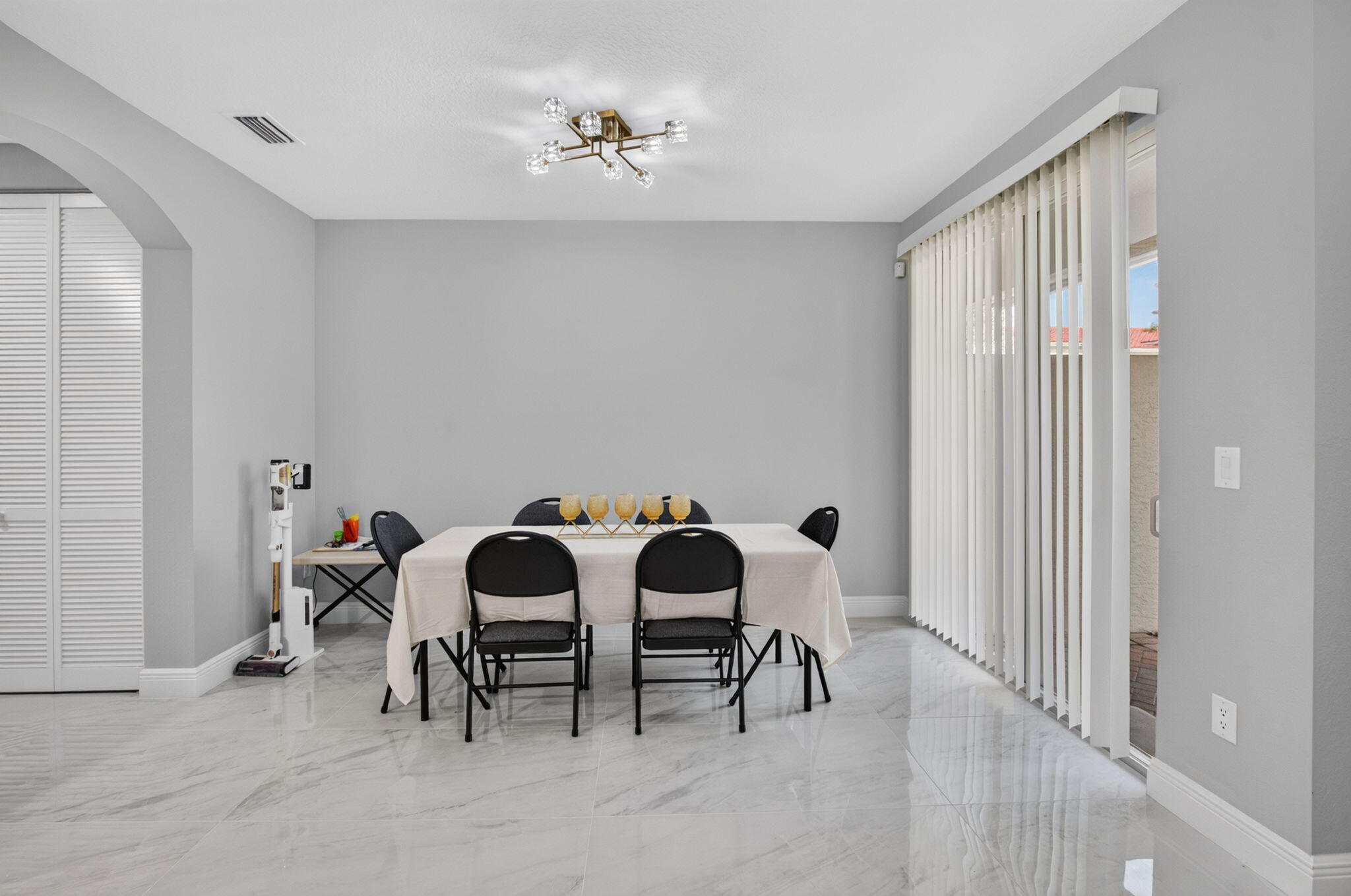 Dining room with a white-clothed table, black chairs, marble-look floors, and sliding glass doors.