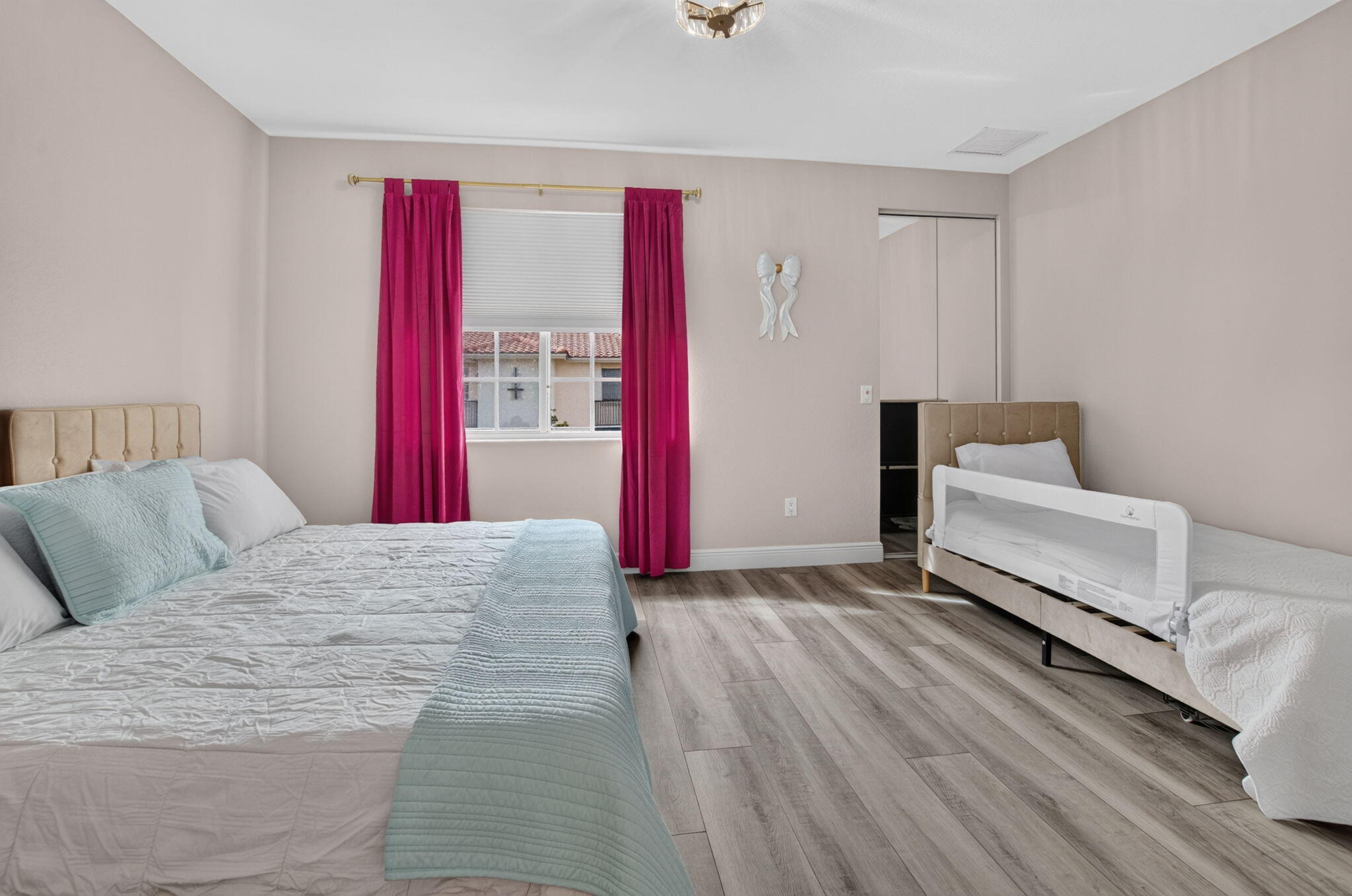 Bedroom with magenta curtains, a large bed, and a second bed with a white safety rail
