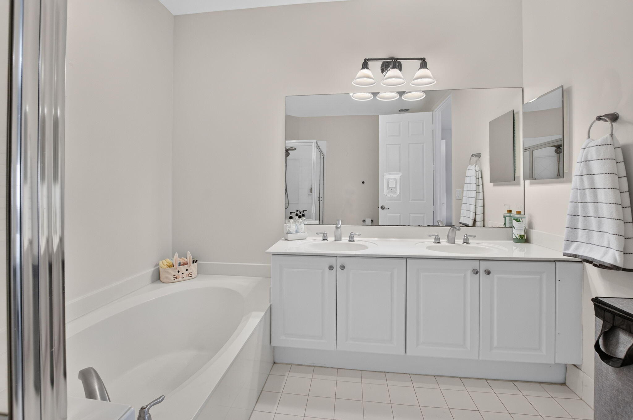 Bathroom with a white double vanity, large mirror, and bathtub beside a glass-enclosed shower.