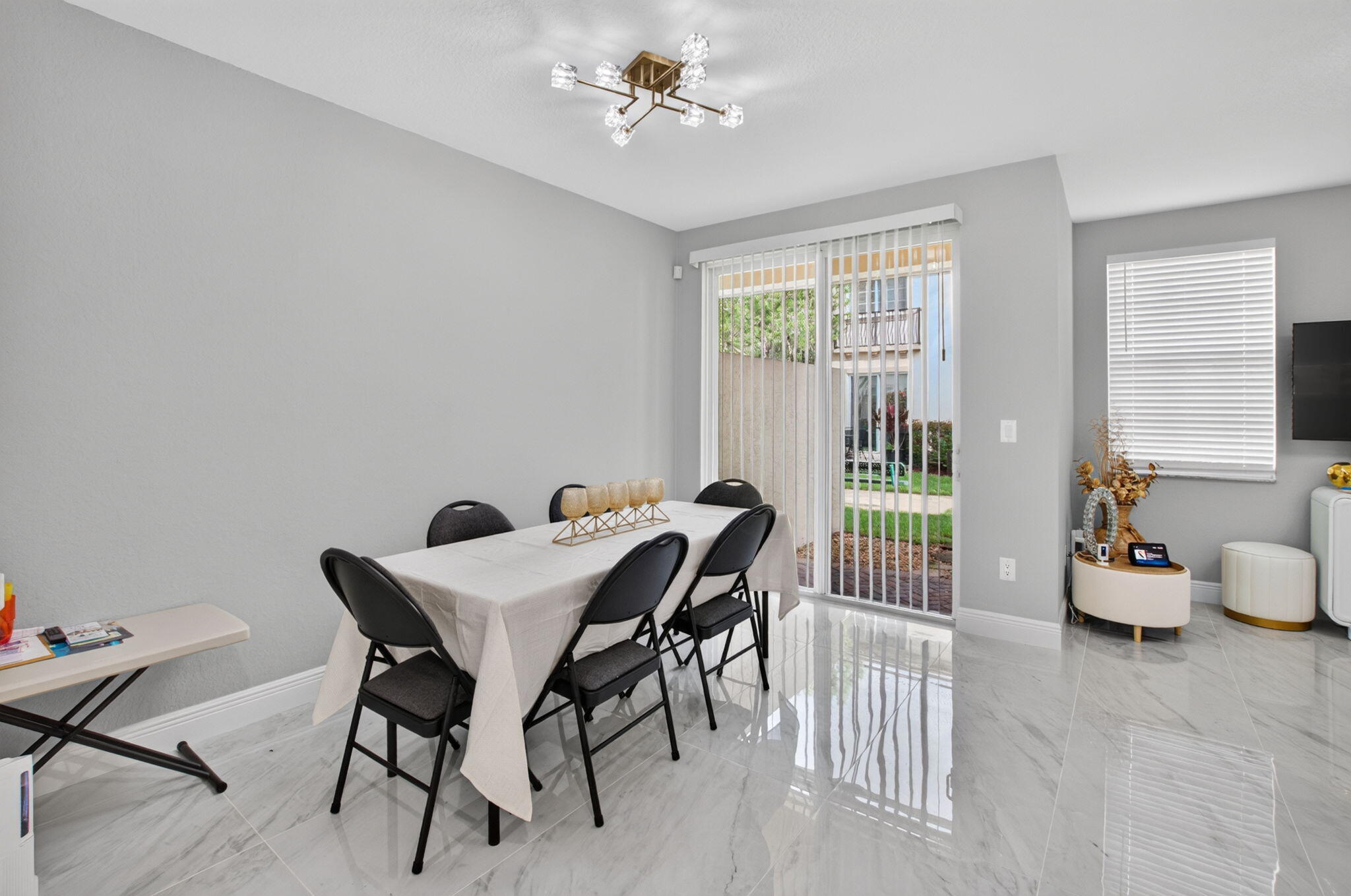 Dining area with a table and black chairs beside sliding glass doors and glossy tile flooring.