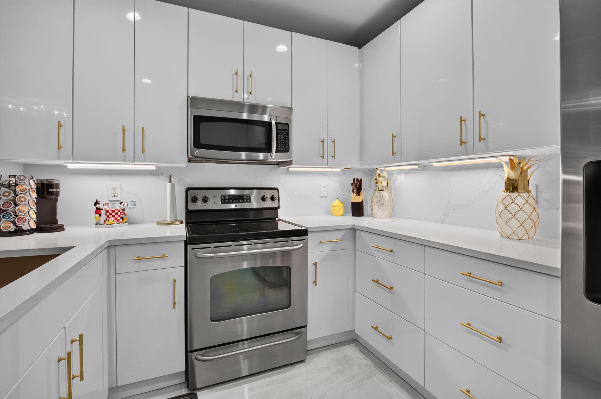Modern white kitchen with gold cabinet pulls and stainless-steel range and microwave.