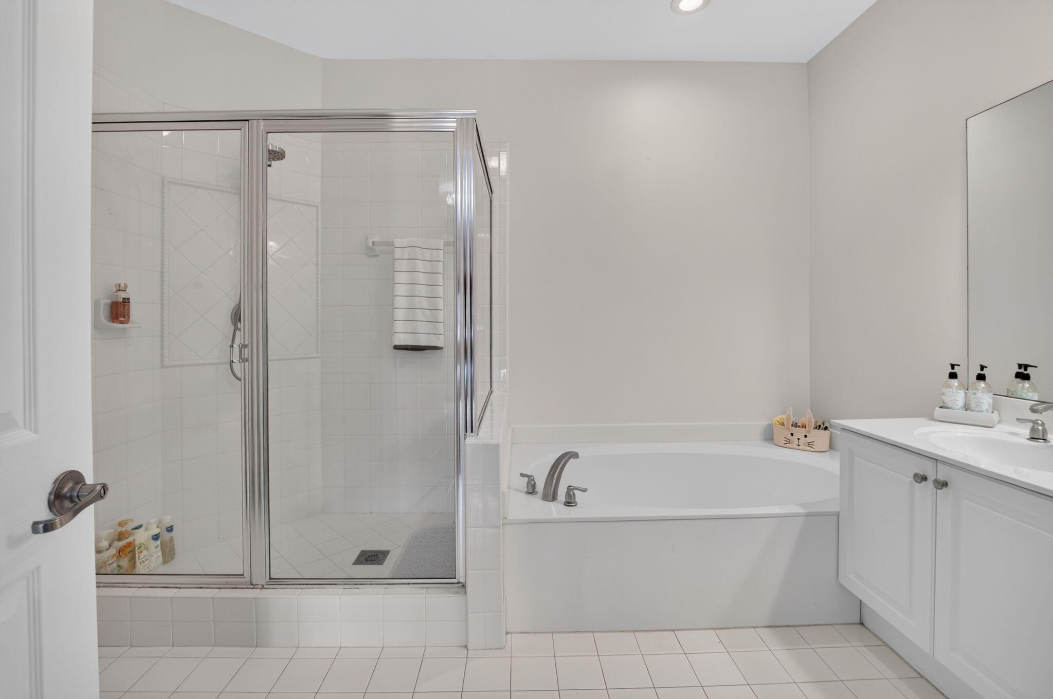 White bathroom with a glass shower, built-in tub, and vanity with sink.